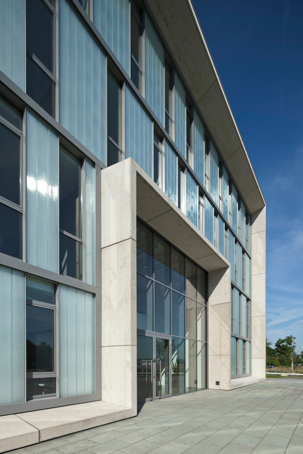 Die Fassade ist gefasst durch einen Rahmen aus hellen Sichtbetonelementen, der sich auch um den Eingang legt