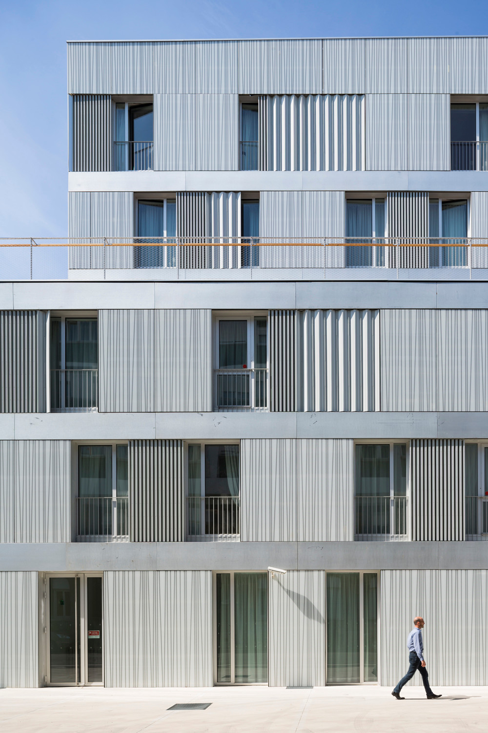 Opake Glasplatten, Aluminium-Profile und Falt-Fensterläden bilden die Fassade des sechsgeschossigen Neubaus