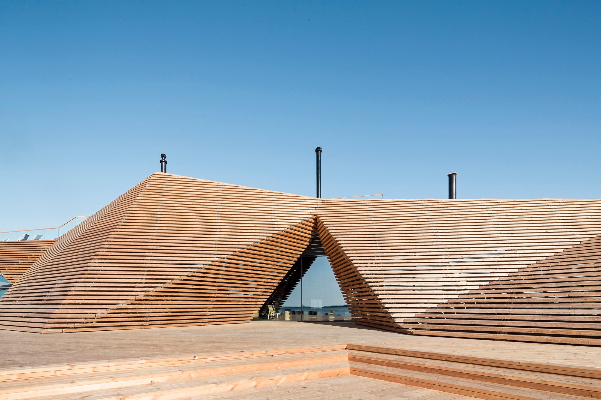 Über den Gebäudekern warfen die Architekten eine Art voluminösen „Mantel“ aus lamellenartig angeordneten Holzbohlen