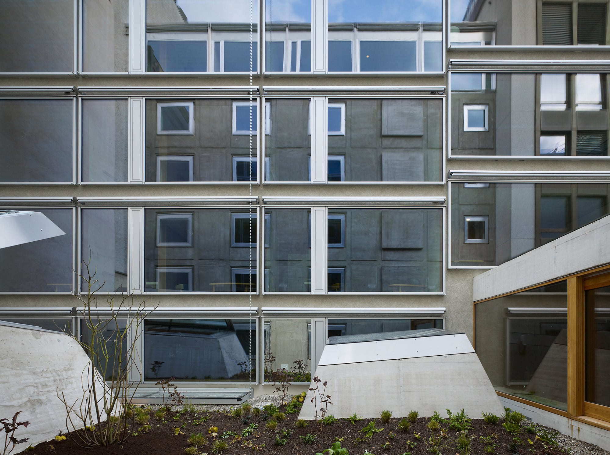 Blick vom begrünten Dach über dem verbindenden Erdgeschoss auf die verglaste Neubaufassade, in der sich der Altbau spiegelt