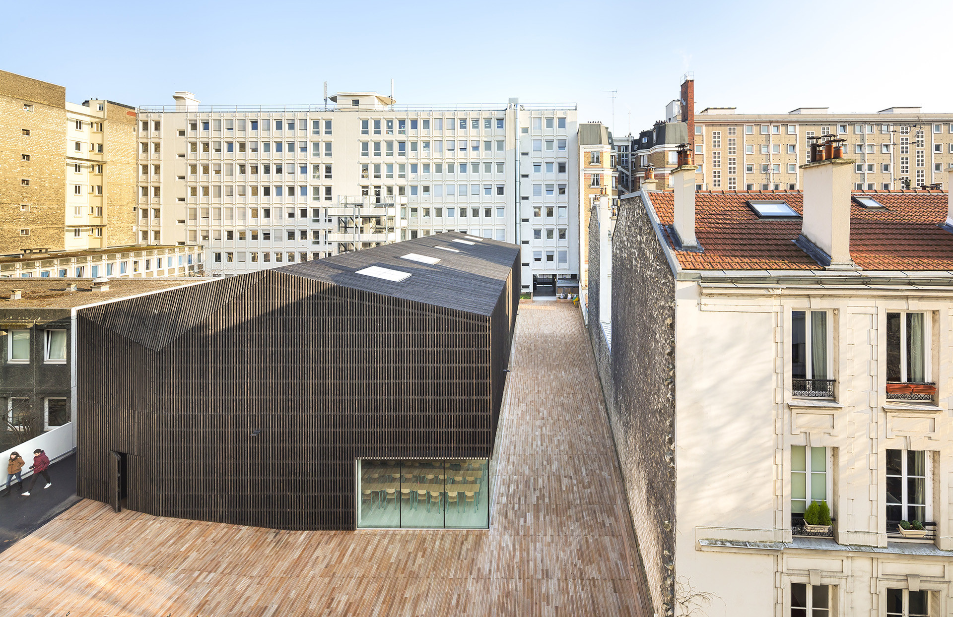 Vertikale, grau-braune Holzlamellen umhüllen das gesamte Gebäude und bilden gleichermaßen Dach und Fassade (Nordwestansicht)