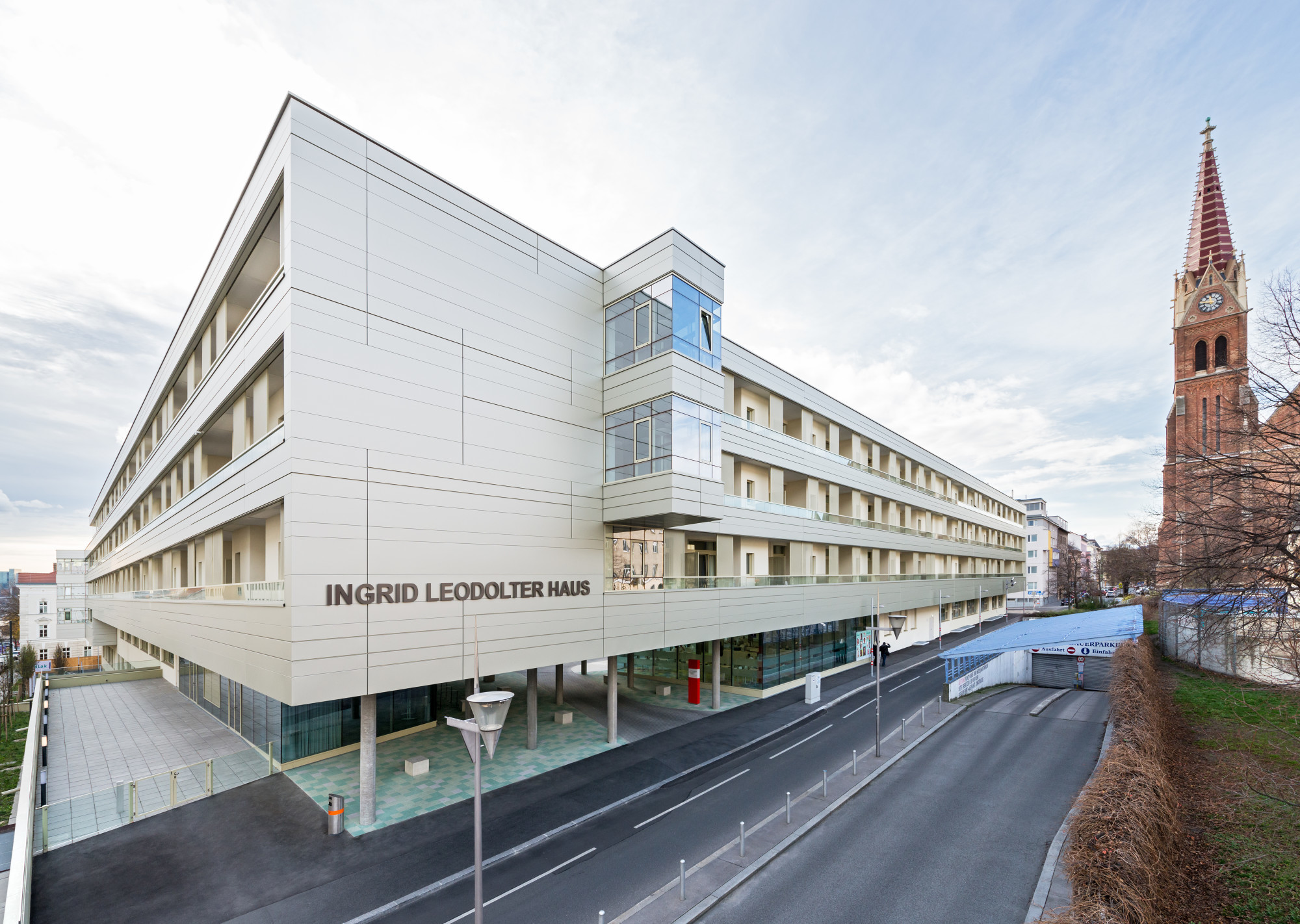 Nordansicht: Den Eingang am Kardinal-Rauscher-Platz markieren grünlich eingefärbte, quadratische Betonbausteine als Pflasterung
