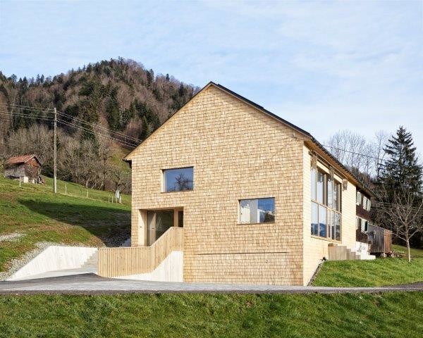 An der Westseite befindet sich der Eingang; kaum sichtbar versteckt sich hinter der Holzschindelverkleidung eine Doppelgarage