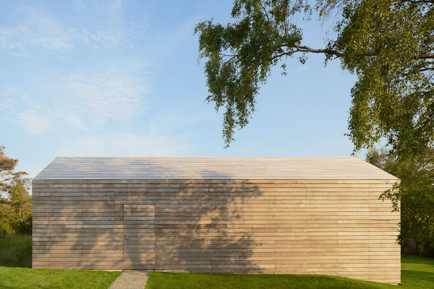 An der Nordseite ist die Eingangstür nahezu unsichtbar in die Fassade aus horizontal angeordneten, massiven Eichenholzbohlen integriert
