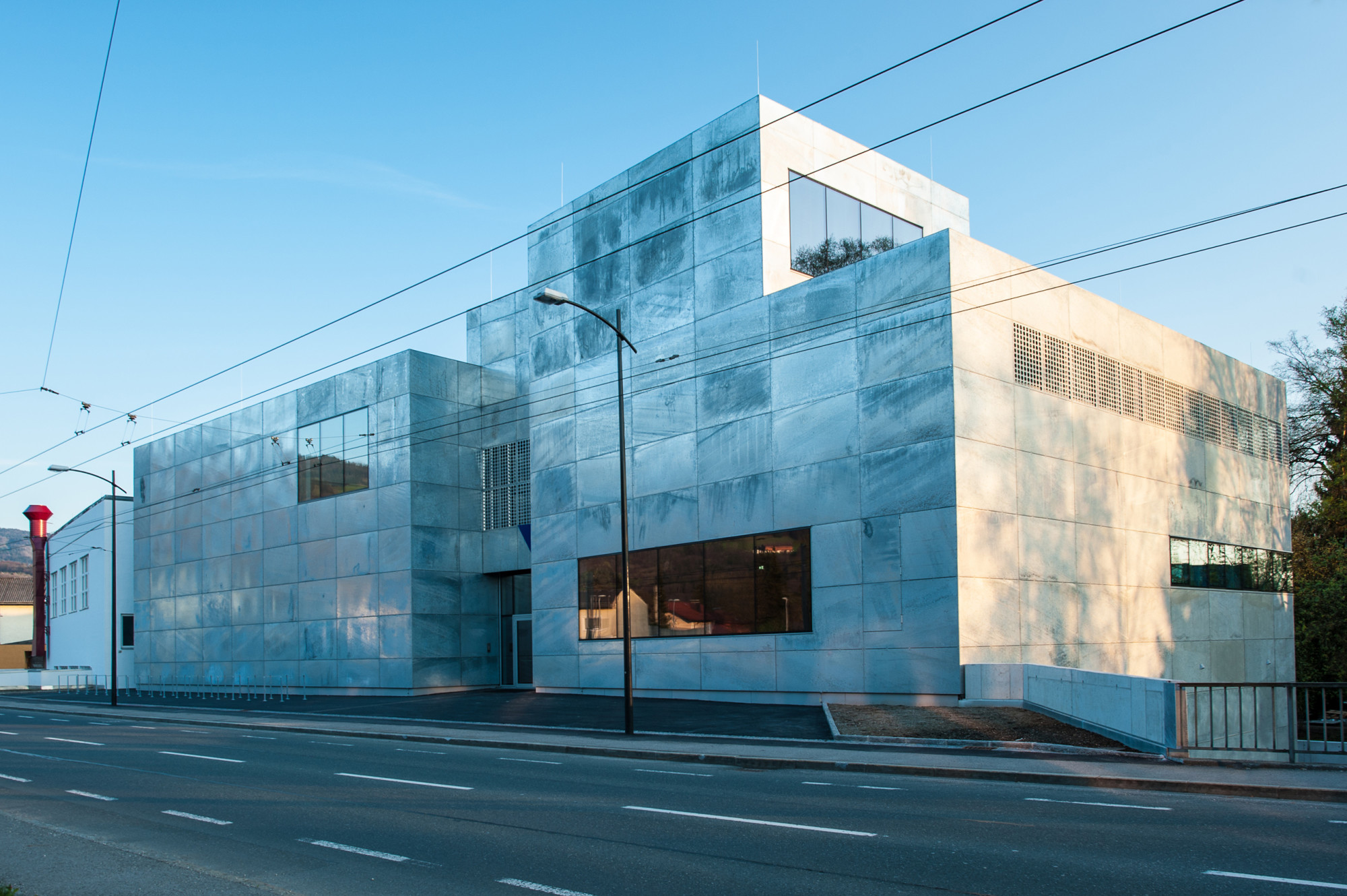 Die Architekturwerkstatt Zopf plante sowohl Sanierung und Umbau des weiß verputzten, bestehenden Werkstattbaus als auch den angrenzenden Neubau mit Metallhülle
