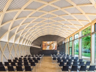 Ein verglastes Foyer verbindet den Konferenzsaal mit dem dunkel bekleideten Lagergebäude (Nordansicht)