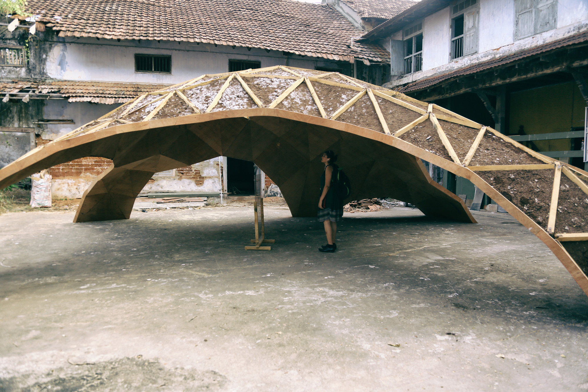 Ein Stabtragwerk aus Holz bildet dreieckige Felder mit Verbindungspunkten aus Metall, die Unterseiten sind mit Sperrholz bekleidet