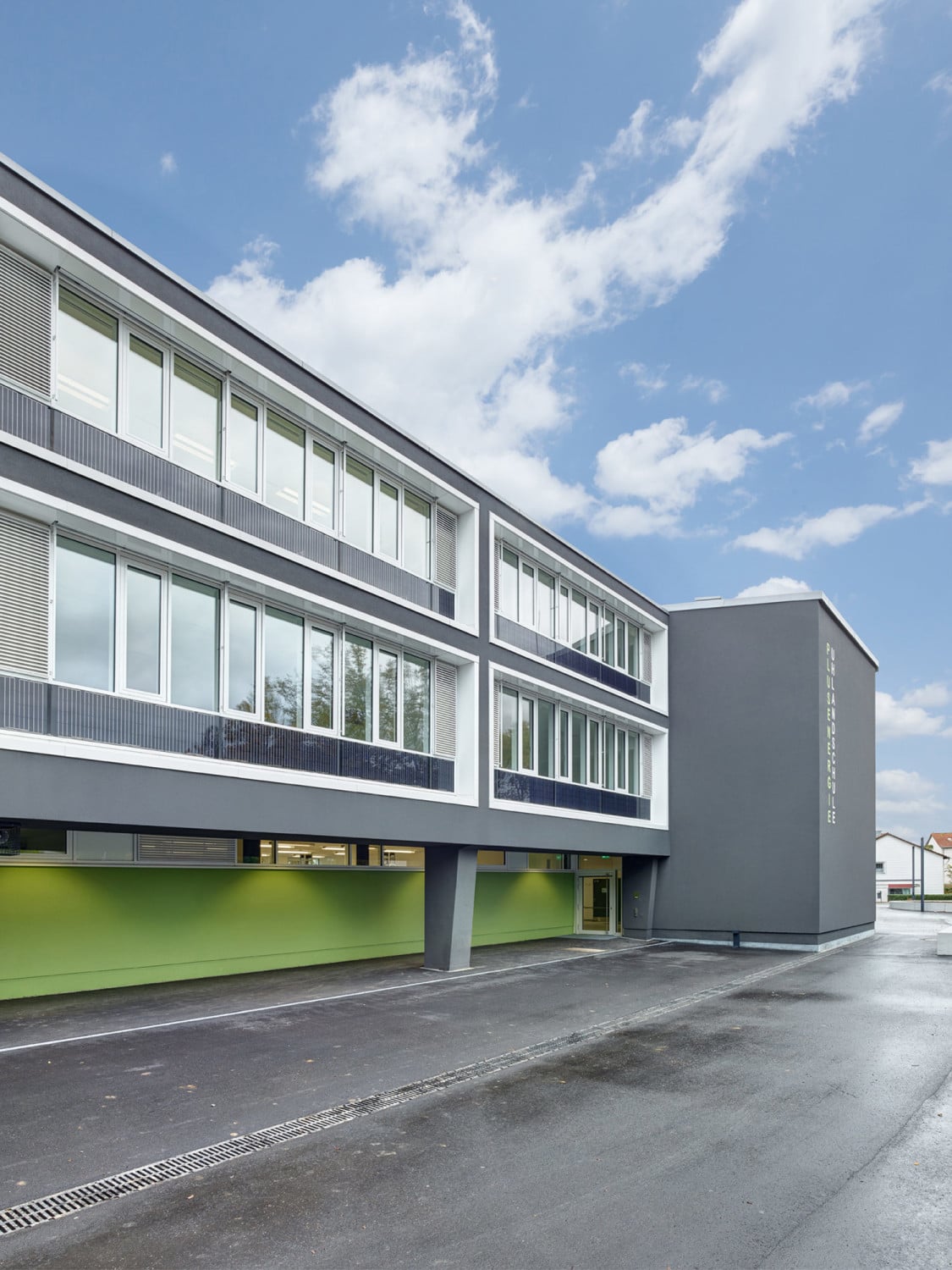 An der Südfassade belichten Fensterbänder die Klassenzimmer, das geschlossene Erdgeschoss springt deutlich zurück, wirkt wegen des intensivens Grüns aber nicht abweisend