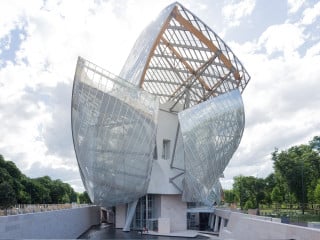 In dem weitläufigen Pariser Stadtpark Bois du Boulogne erhebt sich der geschwungene, von transluzenten Glassegeln umhüllte Baukörper der Stiftung Louis Vuitton