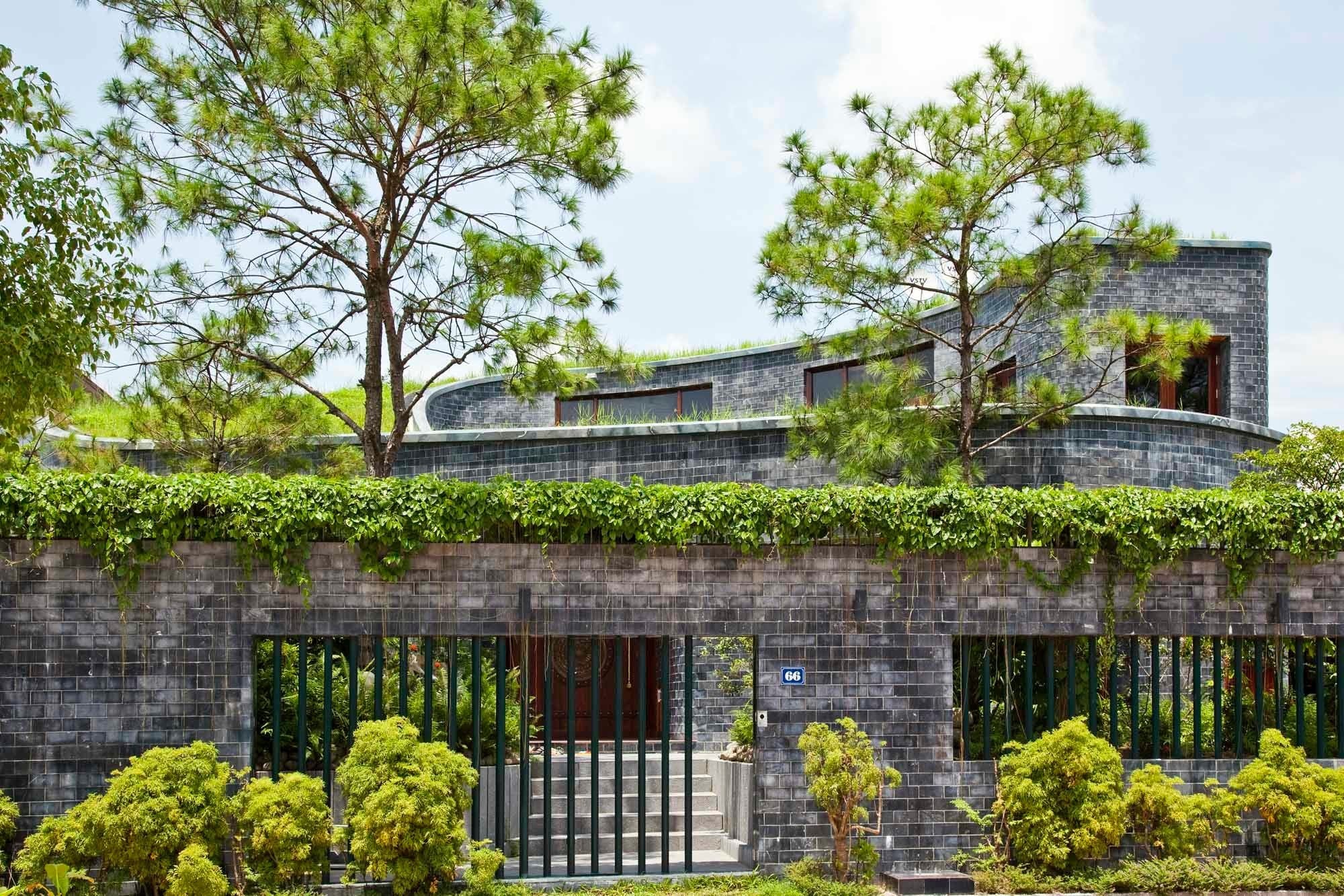 Das steinerne Wohnhaus nach Plänen von Vo Trong Nghia Architects ist durch eine Mauer eingefasst und von üppigem Grün bewachsen