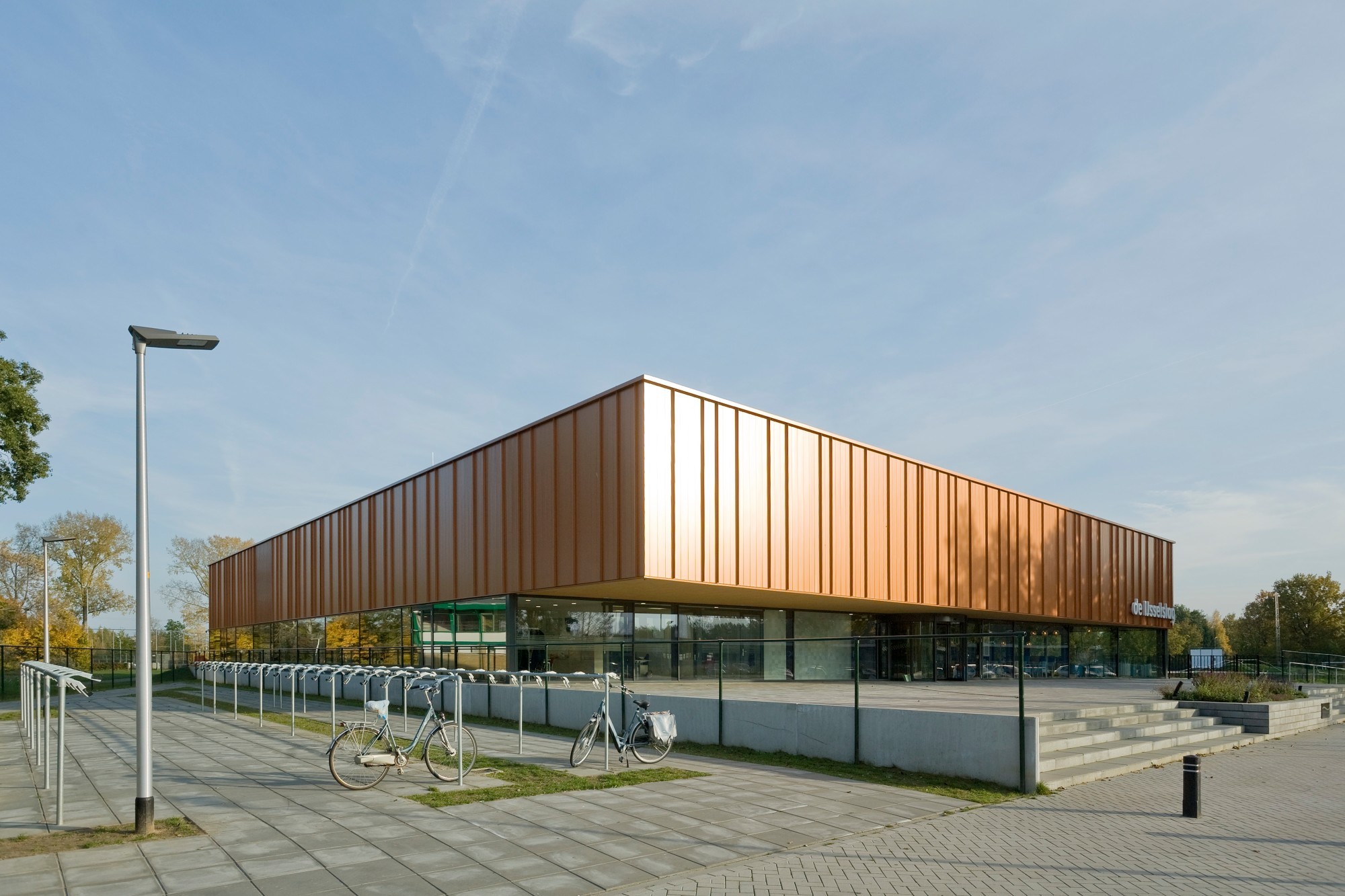 Der Entwurf für den Neubau mit verglastem Sockelgeschoss, einer Bekleidung aus kupferfarbenen Aluminiumplatten und gefaltetem Dach stammt von Slangen+Koenis Architecten.