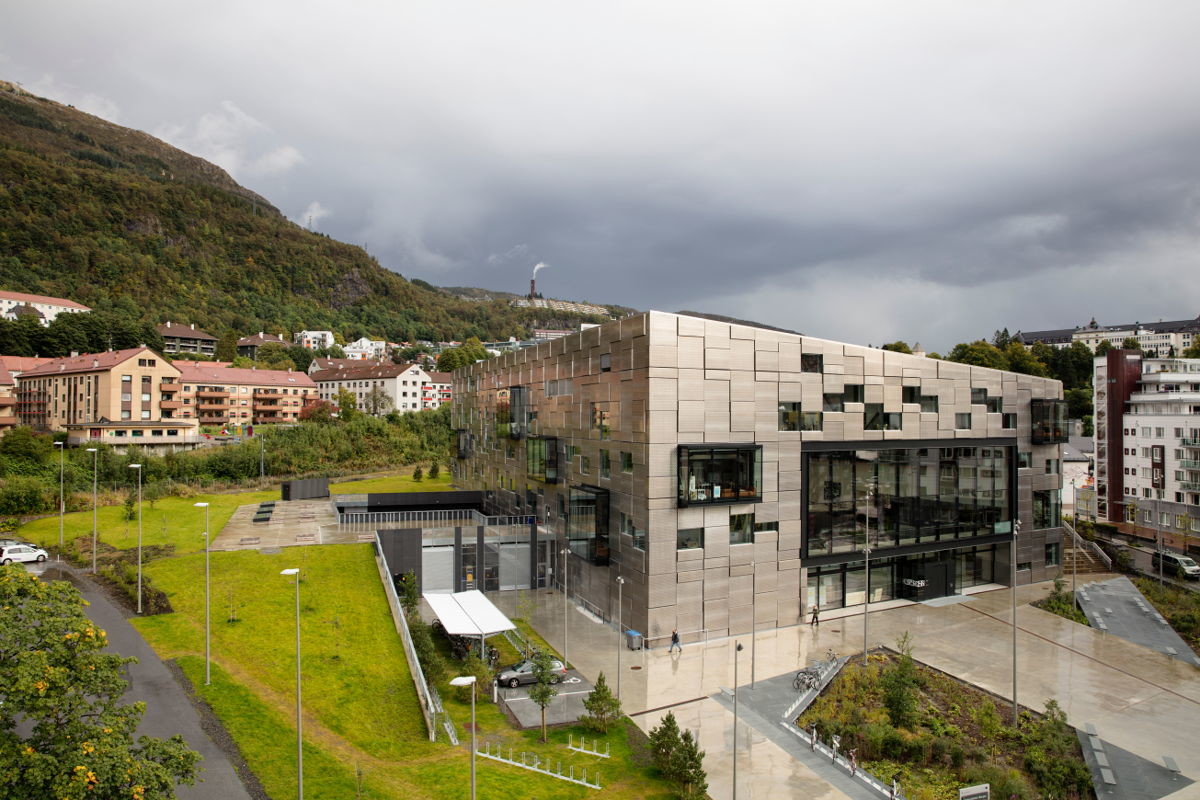 Eine prägnante, im häufigen Regen metallisch glänzenden Aluminium-Glas-Elementfassade umschließt den Baukörper.