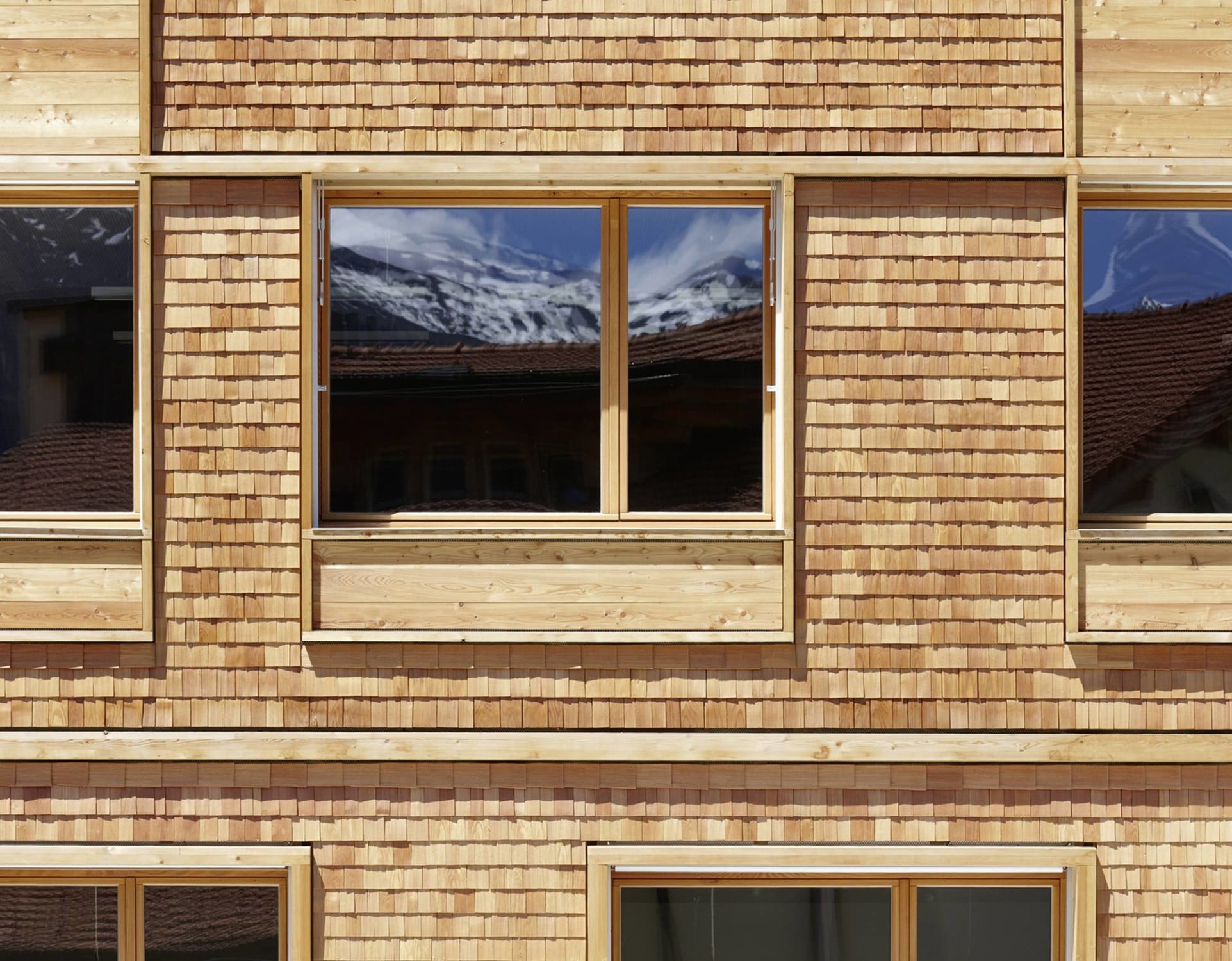 Die handgespaltenen Lärchenschindeln zeugen vom ländlichen Kontext, während die akzentuierten, mit Holzlatten verkleideten Felder unterhalb der Fenster das Haus in der Gegenwart verankern