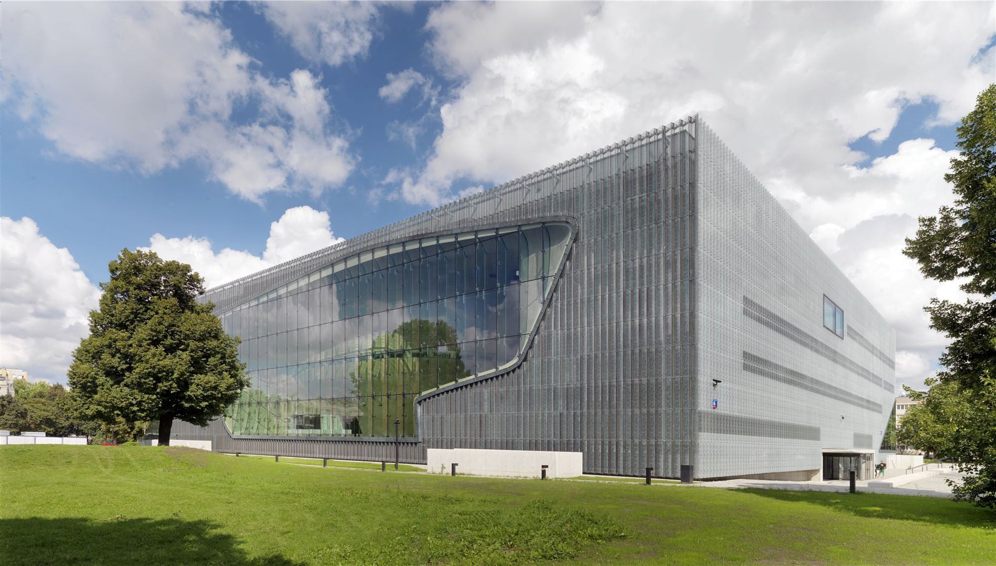 Die Glasscheiben der geschuppten Hülle sind mit Schriftzügen bedruckt; auf der Eingangsseite und zum Park im Südwesten ist die transluzente, vertikal strukturierte Fassade großflächig durchbrochen