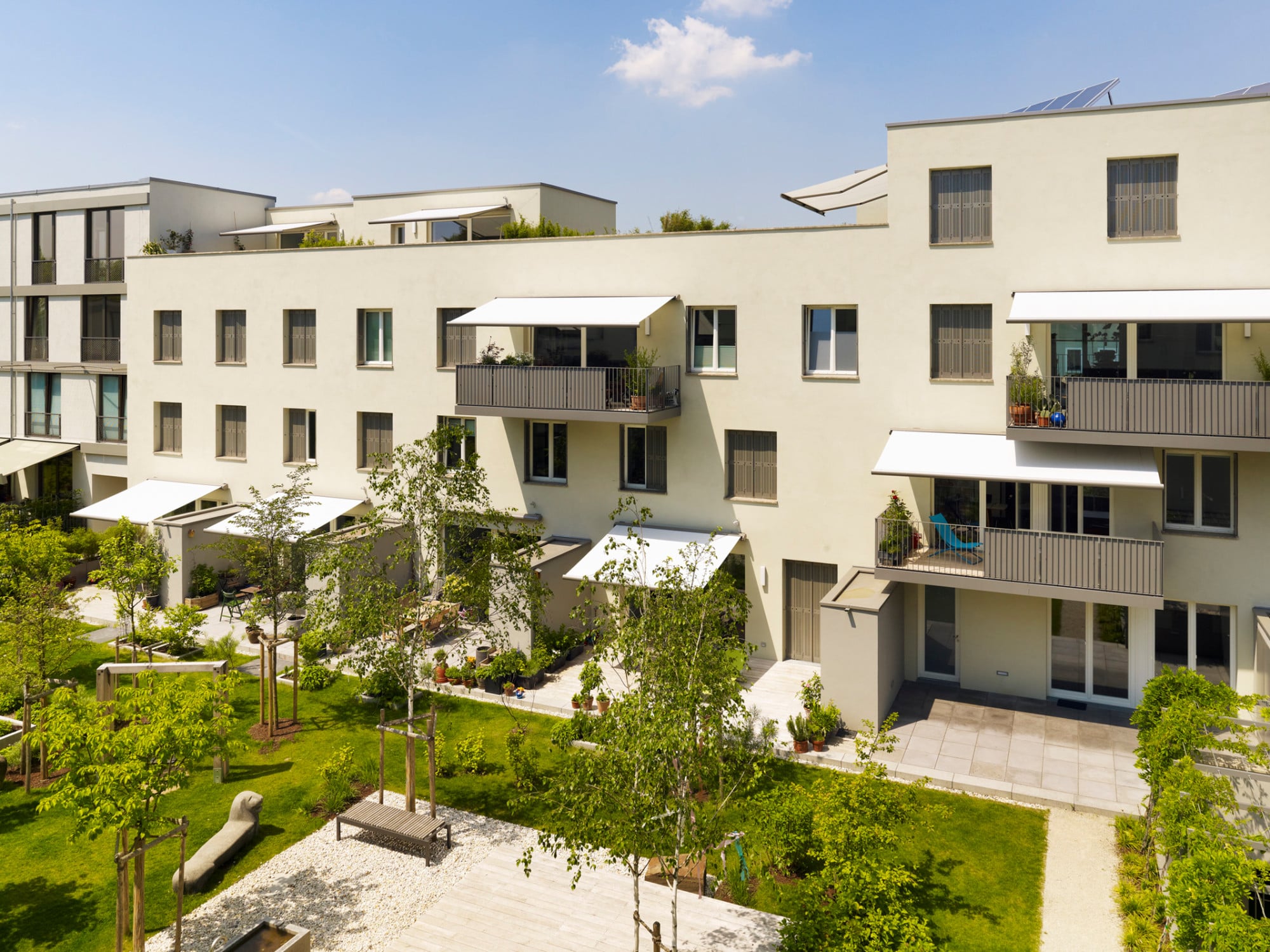 Die Anlage besteht aus zwei parallel verlaufenden, hell verputzten Gebäuderiegeln im Passivhausstandard, zwischen denen ein großer Gemeinschaftsgarten liegt