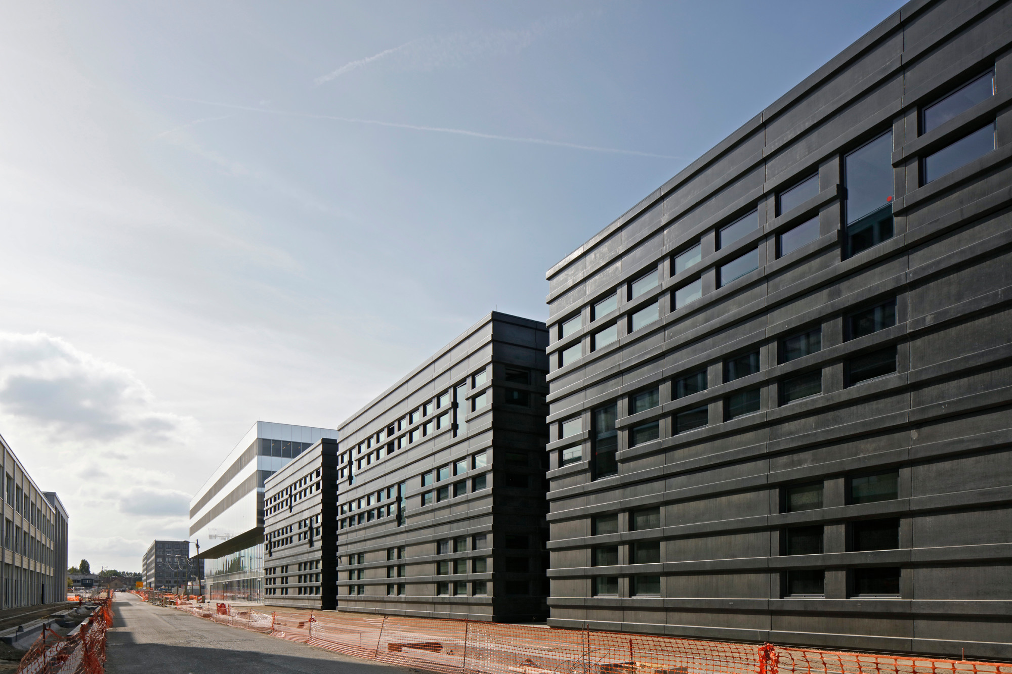 Mit Ausnahme des südwestlichen Blocks mit Glas- und Lochblech-Aluminiumfassade, sind alle Baukörper von dunklen Betonfertigteile umschlossen