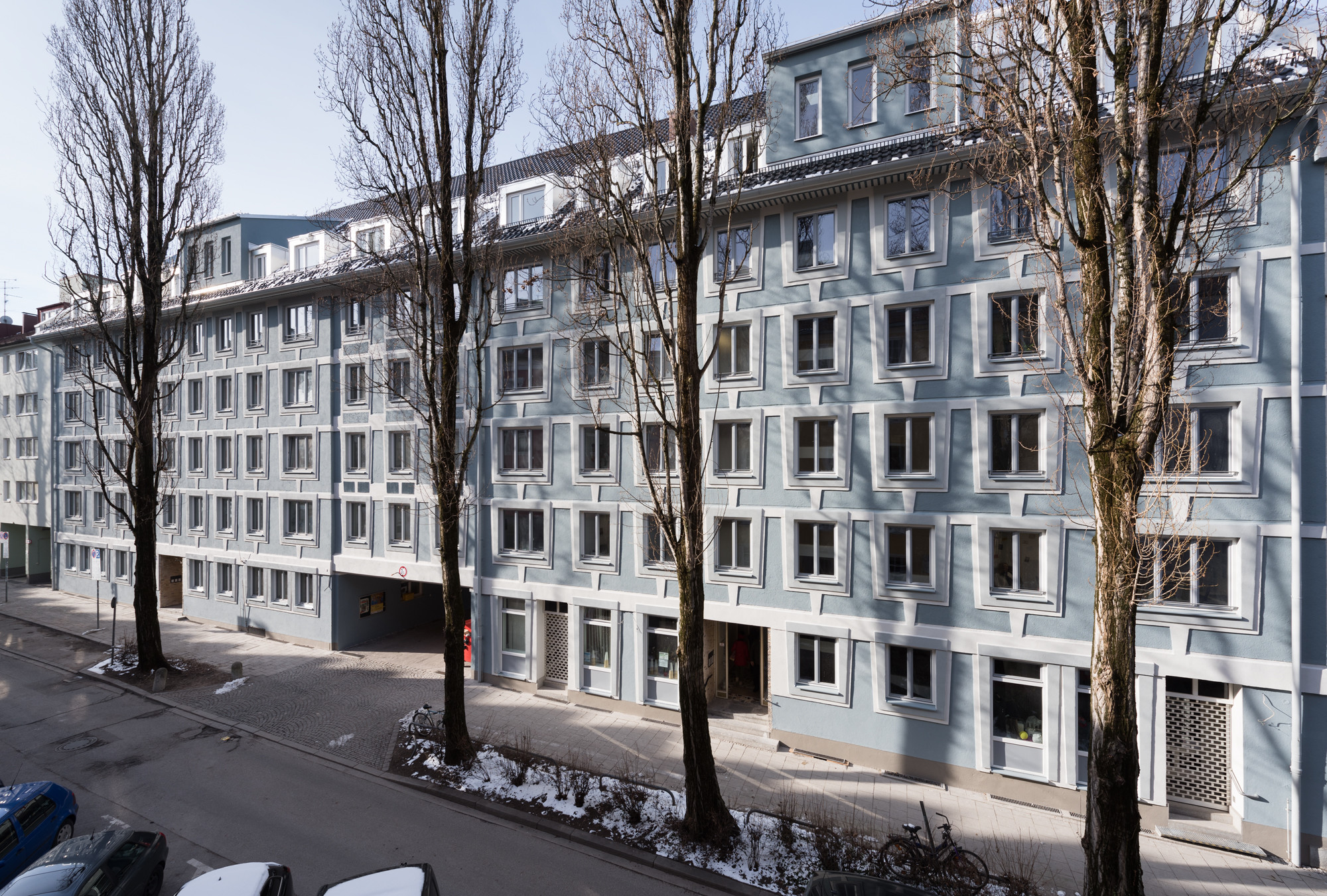 Die zuvor schlicht beige verputze, schmucklose Hülle zeigt sich nach der Modernisierung zur Straße hin in den Farben Hellblau, -grau und Weiß