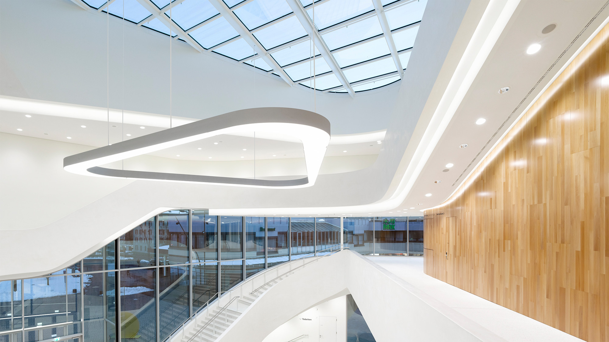 Das lichte Foyer reicht mit seinen weißen Galerien und Lufträumen bis hinauf zur öffentlich begehbaren Dachterrasse; der große Saal hängt wie ein Klangkörper im Gebäude und ist innen- und außenseitig holzverkleidet