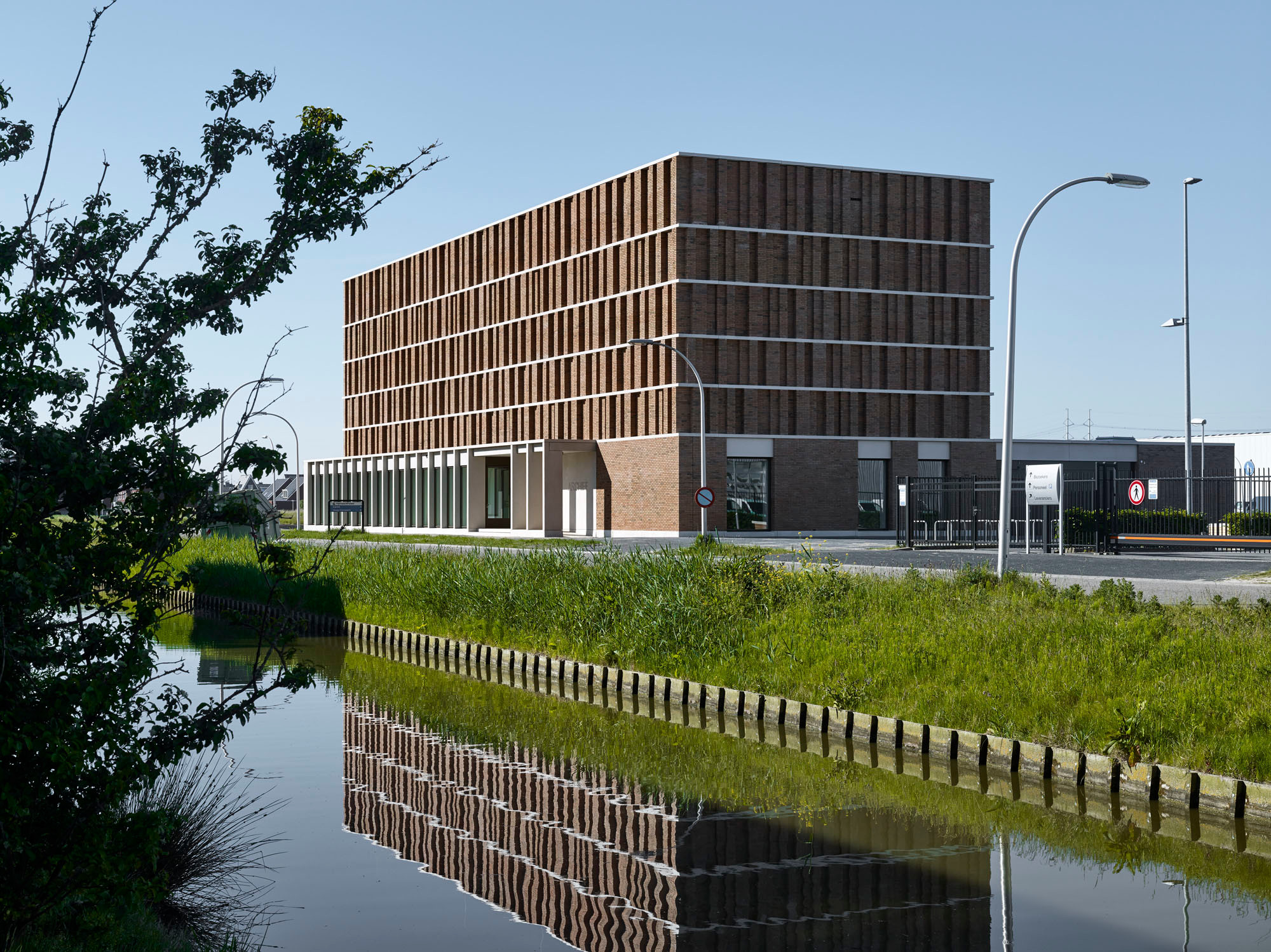 Die Fassade aus rötlich-braunen Klinkern ist in der Horizontalen durch helle, umlaufende Betonbänder gegliedert