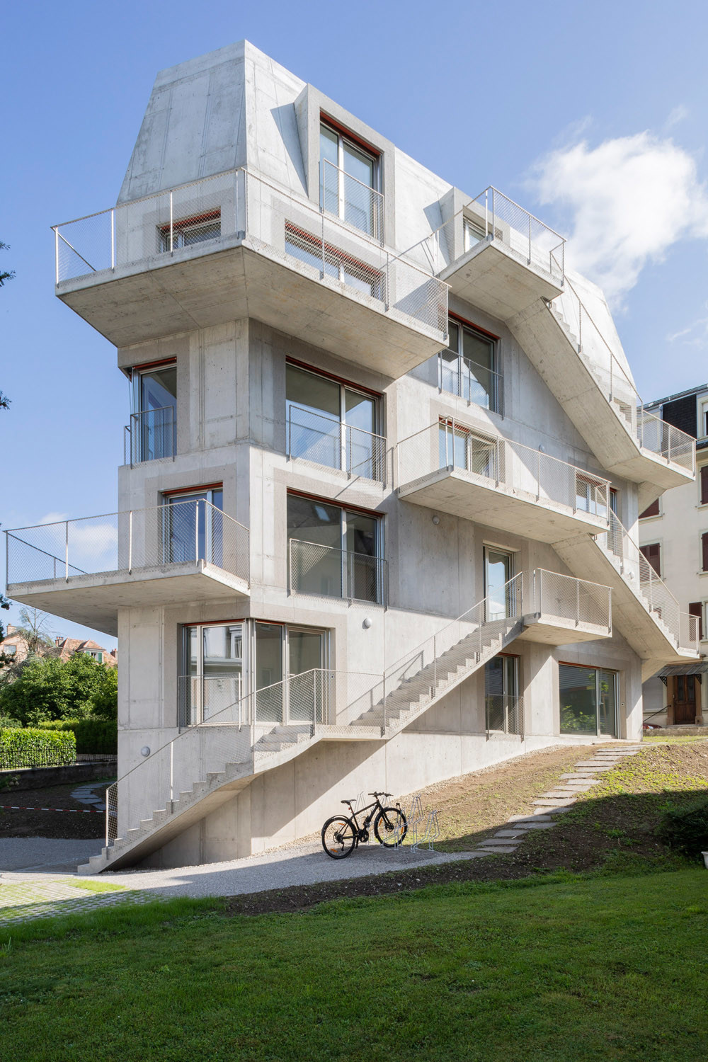 Maximierte Wohnfläche: Drei außen an der Fassade verlaufende Treppen führen zu den Wohneingängen und prägen die Ansicht, ebenso die auskragenden Balkone