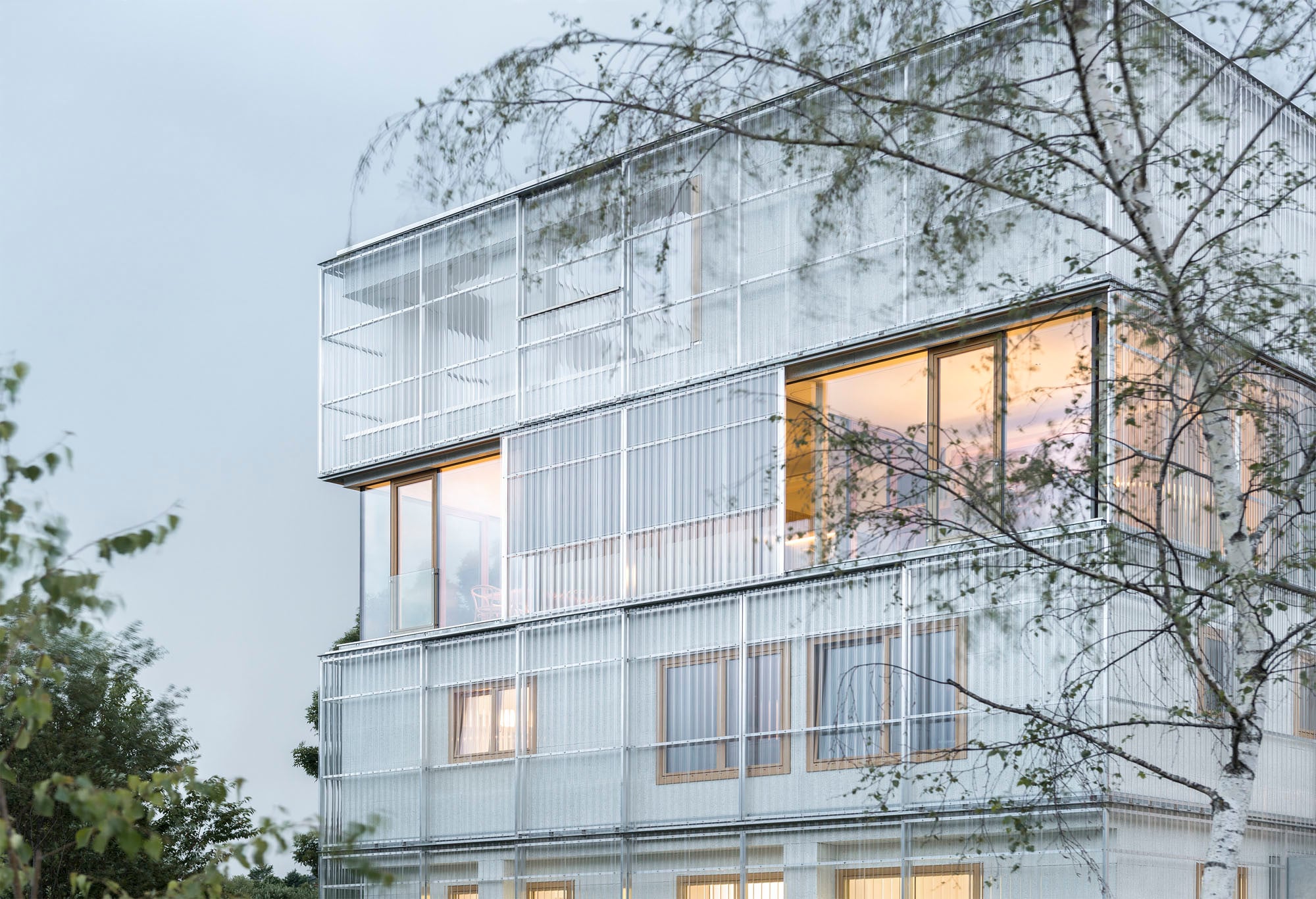 Der zweigeschossige Bestandsbau, ein ehemaliger Handwerksbetrieb, wurde um zwei Ebenen aufgestockt, und das neue Volumen umhüllt mit transparentem gewellten Plexiglas
