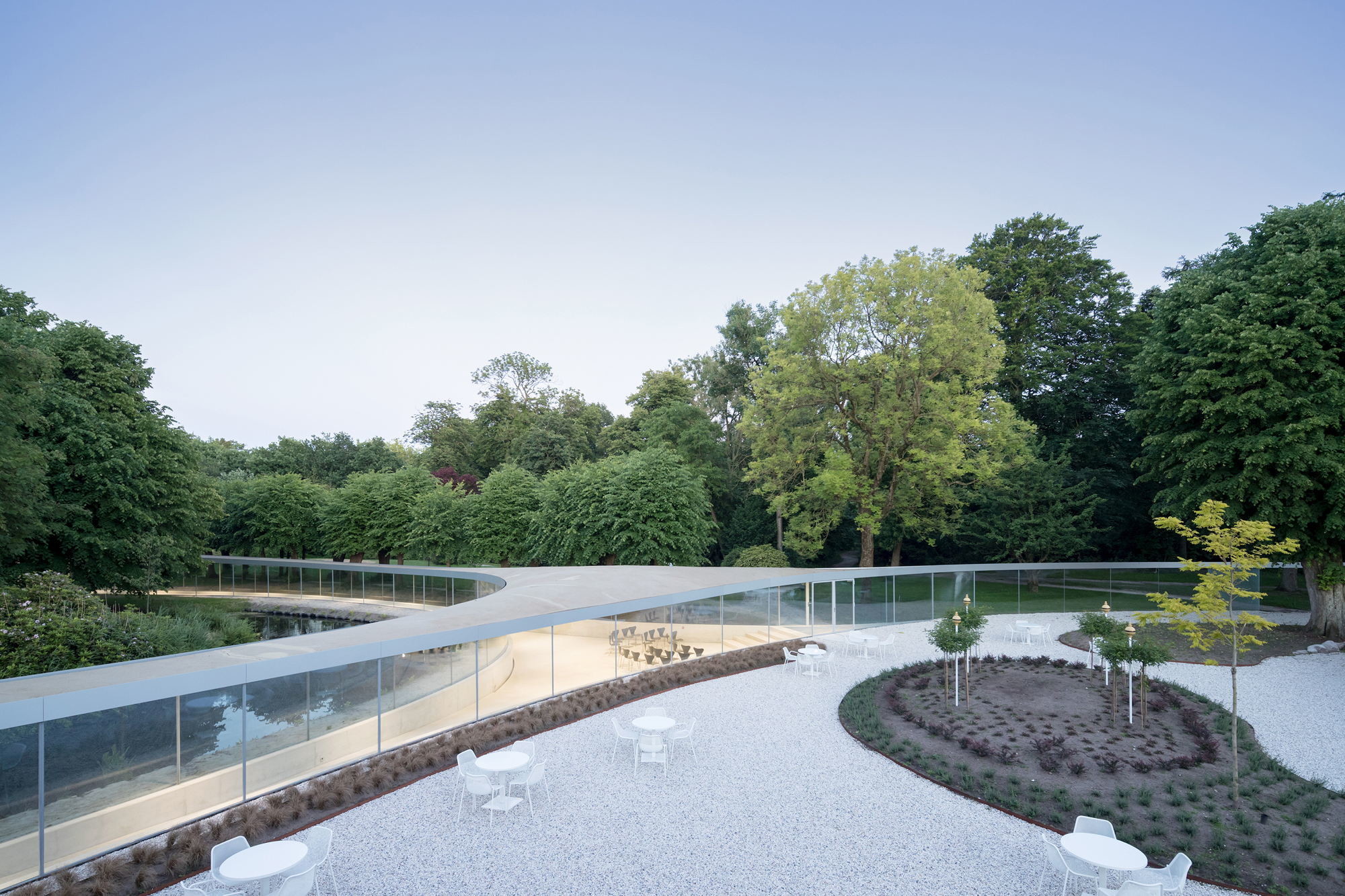 Von einem annähernd dreieckigen Veranstaltungssaal führen drei tentakelartige Arme in die Gartenlandschaft und zum Hauptgebäude.