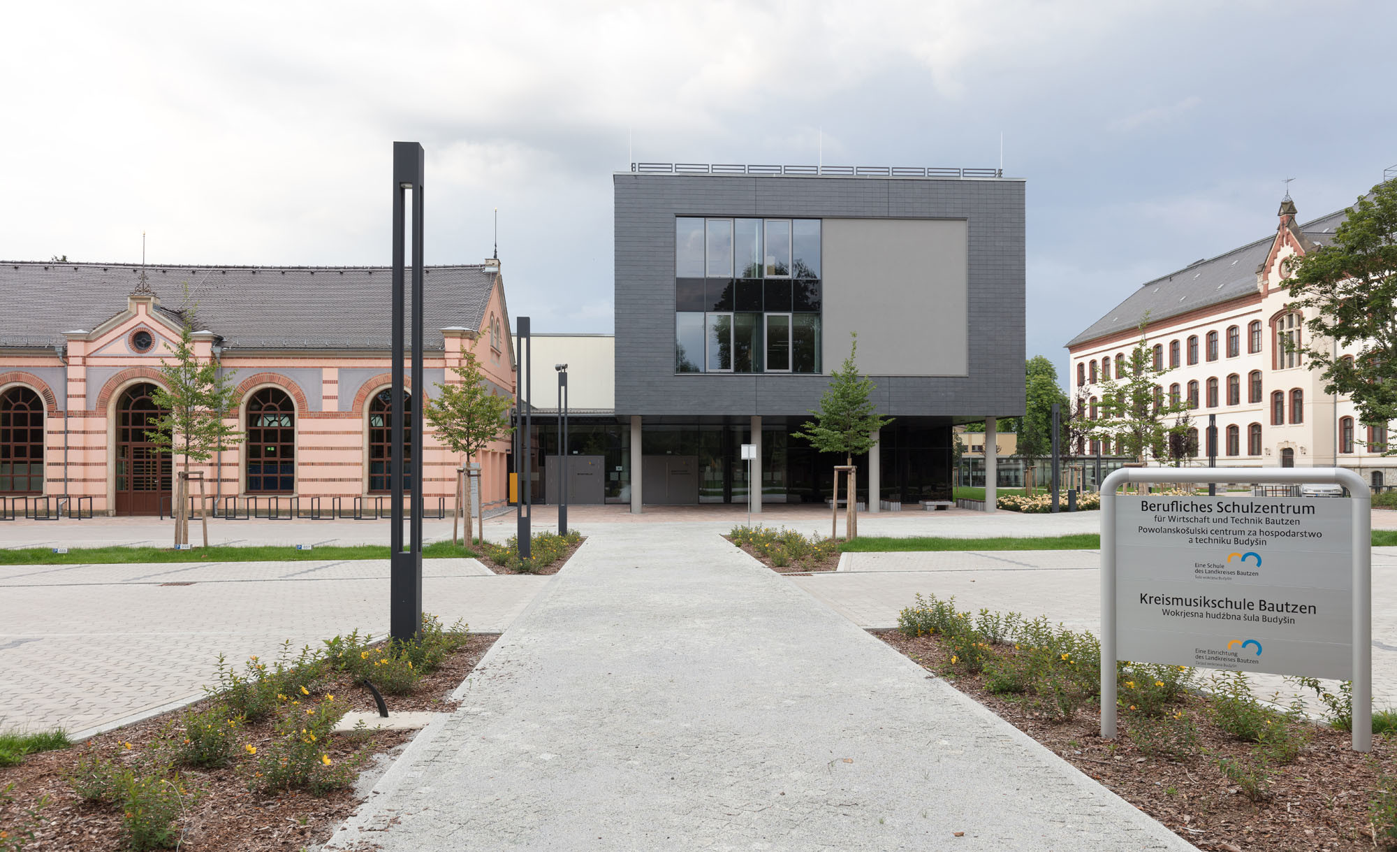 Der nördliche Kopfbau ist aufgeständert; An die benachbarte Turnhalle schließt der Neubau rückwärtig etwas niedriger an