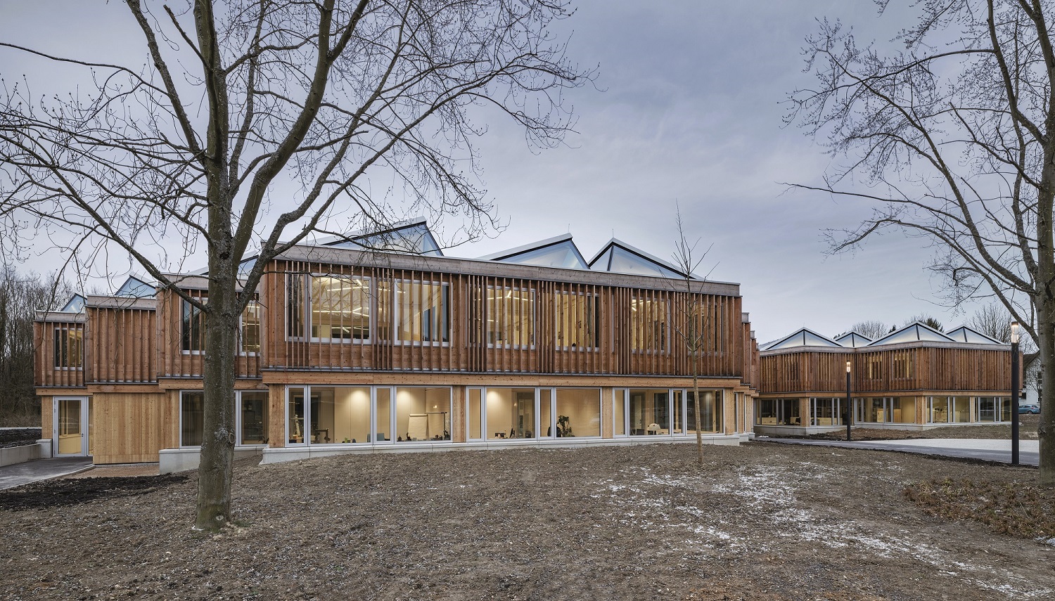 Die gestaffelten Außenwände des Holzskelettbaus und seine kleinteilige, zum Himmel geöffnete Dachlandschaft sorgen für die gute Einbindung des ausgedehnten Gebäudekomplexes.