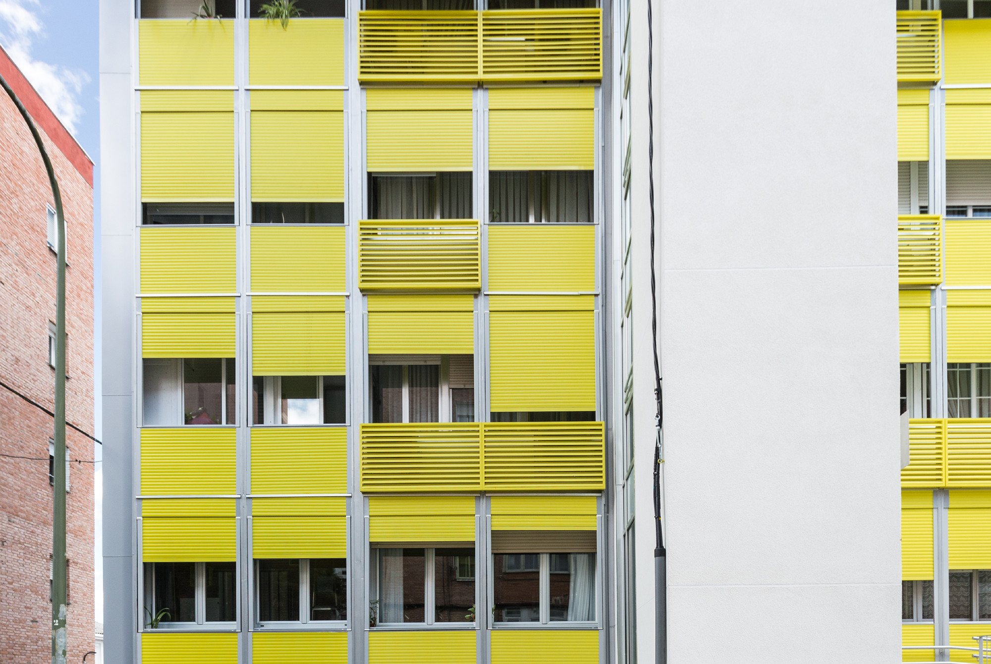 Die Vorhangfassade besteht aus Aluminiumprofilen, die mit knallgelben Aussteller-Rolläden und feststehenden Horizontallamellen ausgefacht sind.