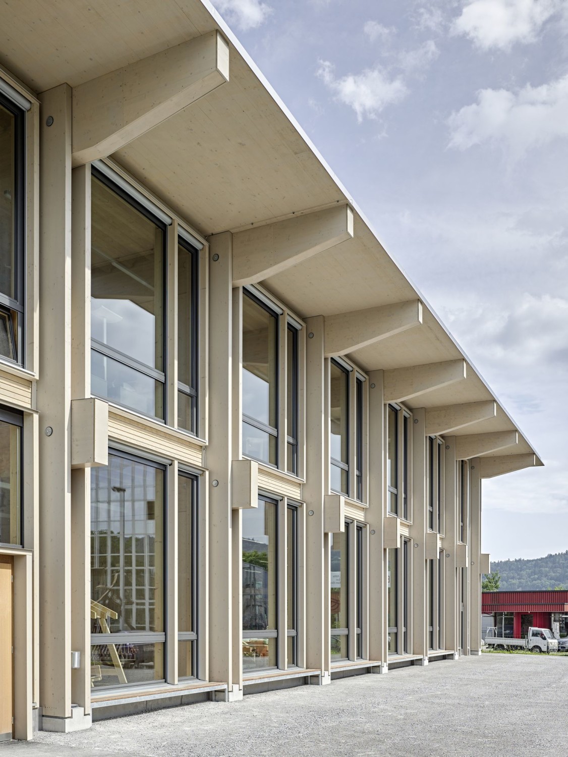 Zwillingsstützen in der Fassadenebene halten die Träger von Dach und Geschossdecke und rastern die Fassade in gleichmäßige Felder mit großzügigen Fensteröffnungen.