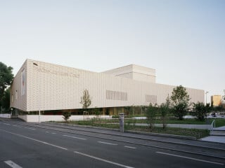 Die Westseite des hell umhüllten Theaters Jacques Carat in Cachan, das einen historischen Theatersaal integriert, richtet sich zu einem städtischen Vorplatz.