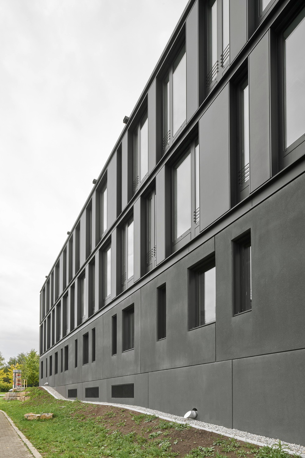 Henning Larsen Architects hüllten den Baukörper ganz in Schwarz: Im Sockel bilden großformatige, schwarz durchgefärbte Sichtbeton-Fertigteile die Fassade aus, in den Obergeschossen eine eloxierte Aluminiumverkleidung, in welche die PV-Module integriert sind.