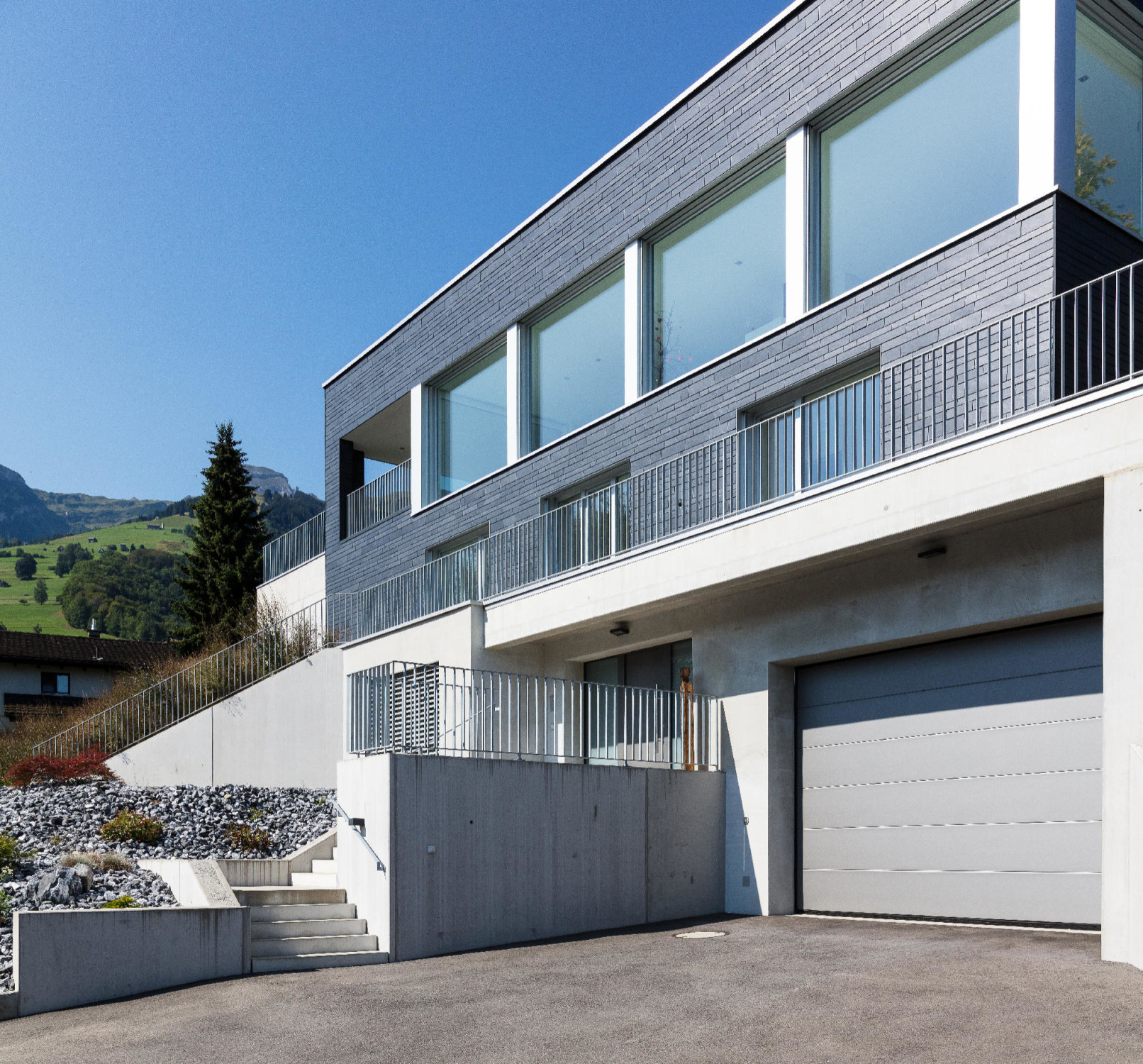 Eingang und Garage befinden sich im Betonsockel, darüber sitzt ein mit Schiefer bekleideter Holzbau.