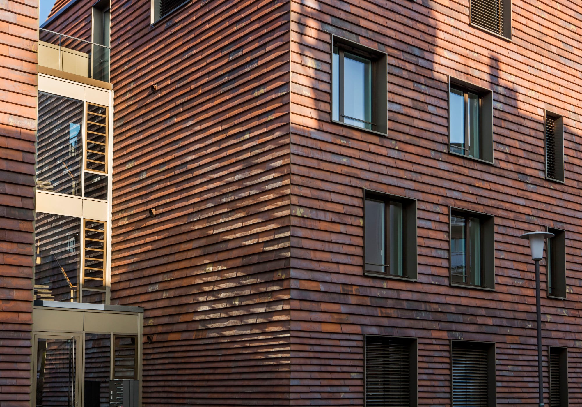 Trotz dieser formalen Angleichung sind die Neubauten durch ihre Fassadenbekleidung aus rot-braunen Keramikplatten und die großen Fenster gestalterisch klar in der Gegenwart verankert.
