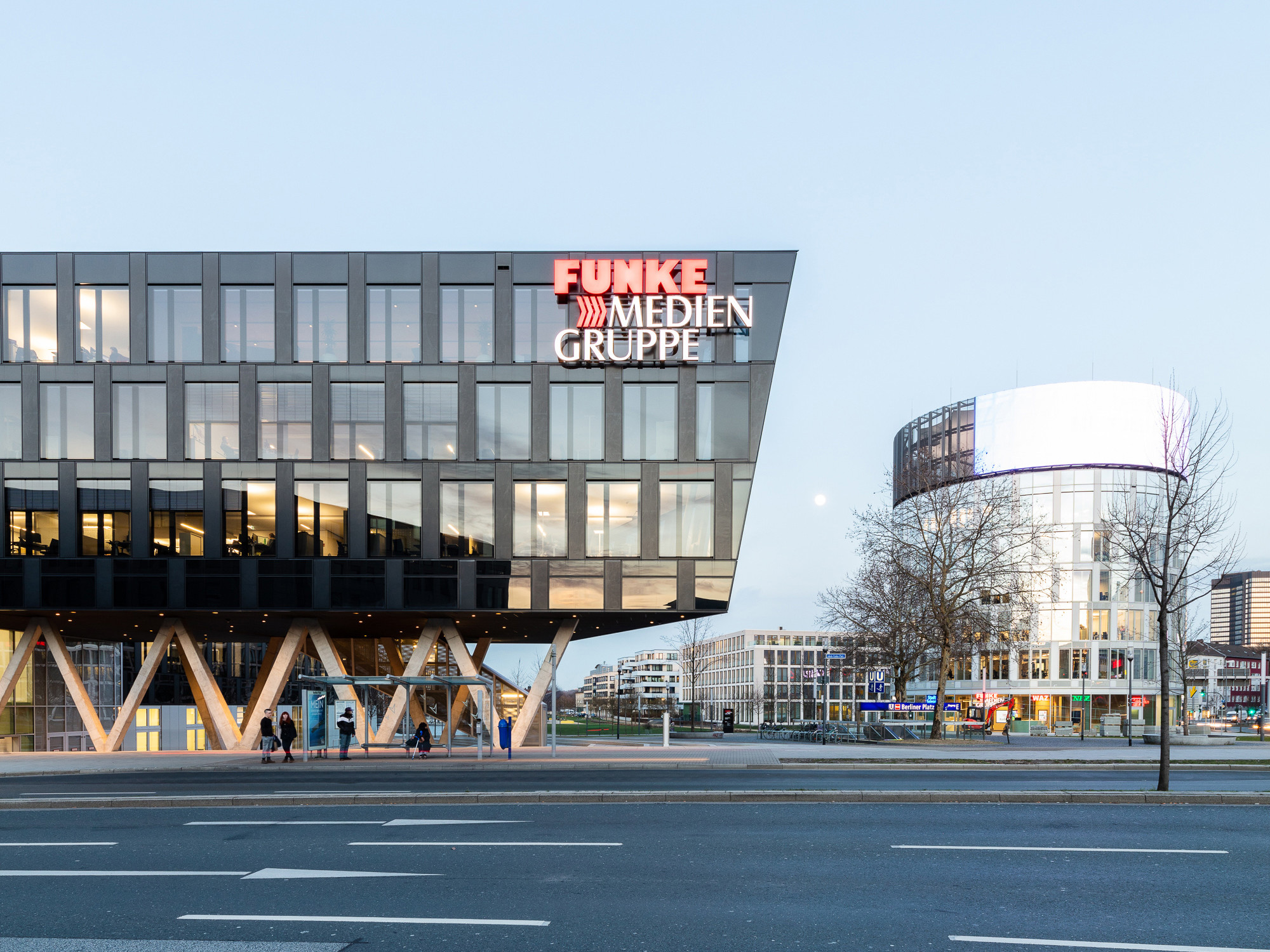 Der Neubau besteht aus einem fünf- bis sechsgeschossigen Riegel mit dunkler Glasfassade und dem Medienturm mit silberfarbener Hülle, der als Kopf des Ensembles wirkt und mit einer großflächigen Medienfassade aufwartet.