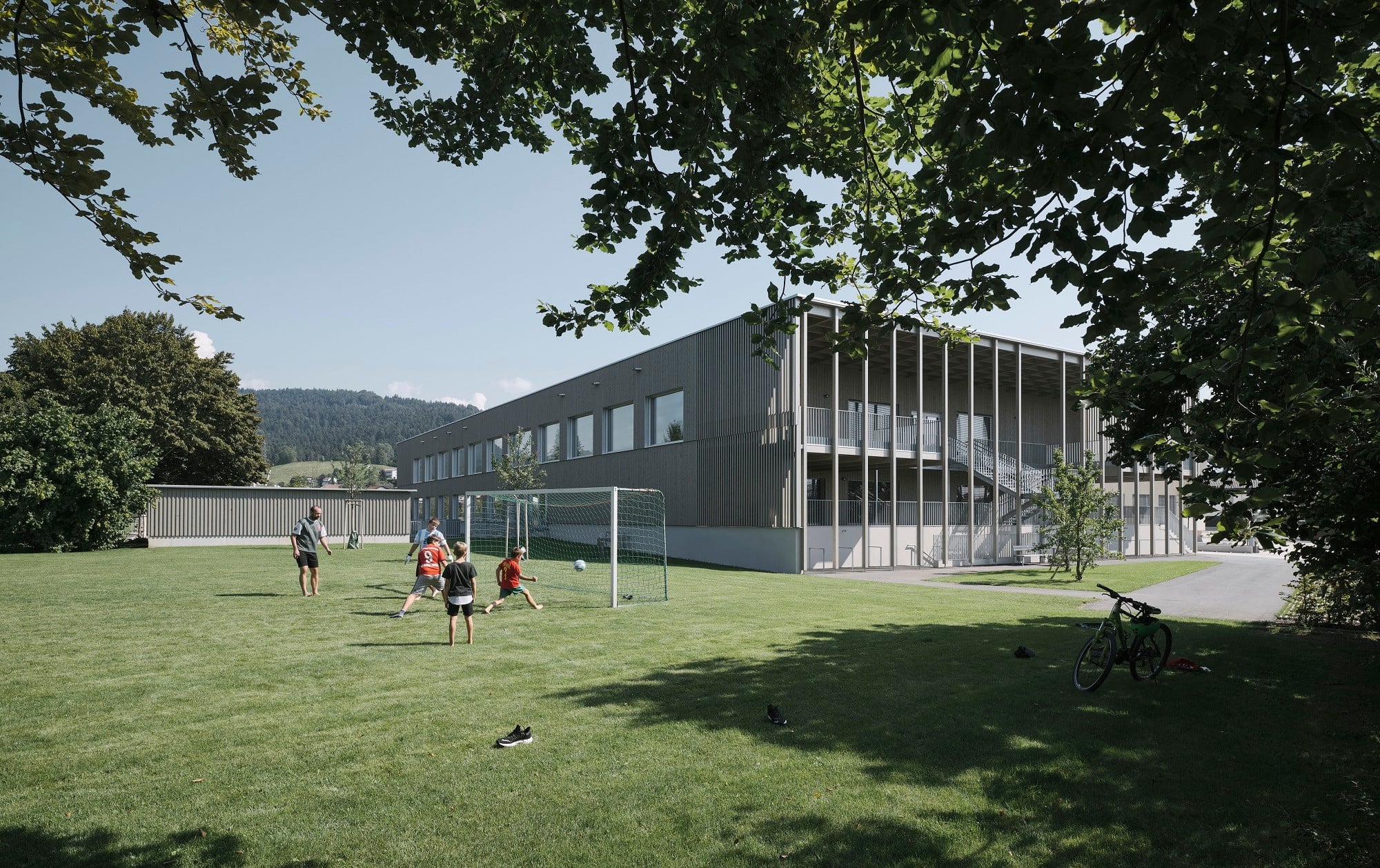 Im Nordwesten befinden sich die Außensportanlagen. Veranden an den Stirnseiten des Neubaus bieten geschützte Spielflächen.