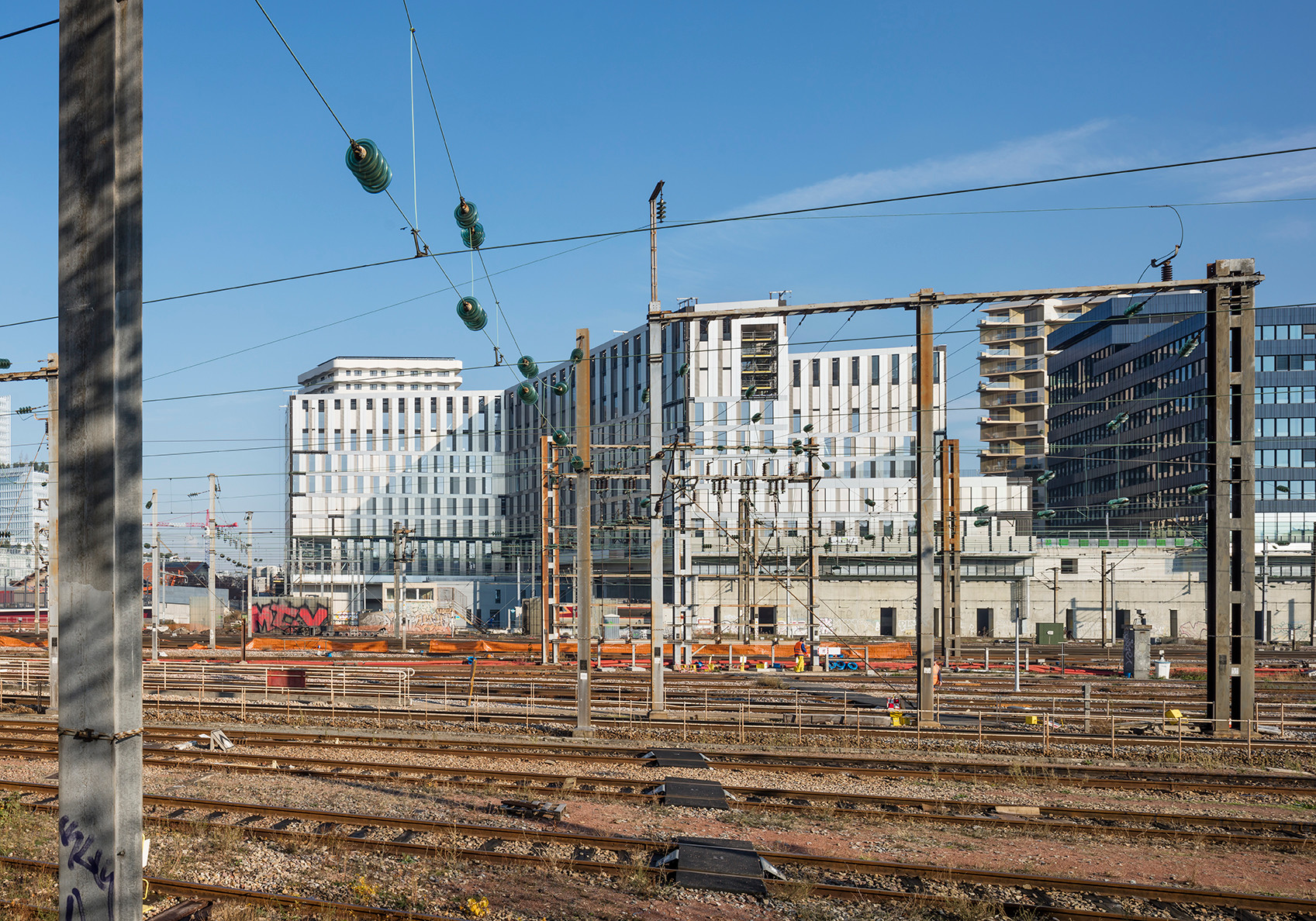 Errichtet auf einem bereits vor zehn Jahren angelegten, brückenartigen Betondeckel, der eine Bahntrasse überspannt, bildet der Neubau einen Hochpunkt und markiert den Zugang zum Quartier.