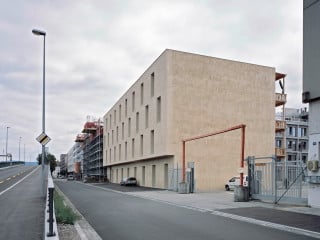 Der quaderförmige Baukörper nach Plänen von Degelo Architekten präsentiert sich straßenseitig mit einer schlichten, beigefarben verputzen Fassade.