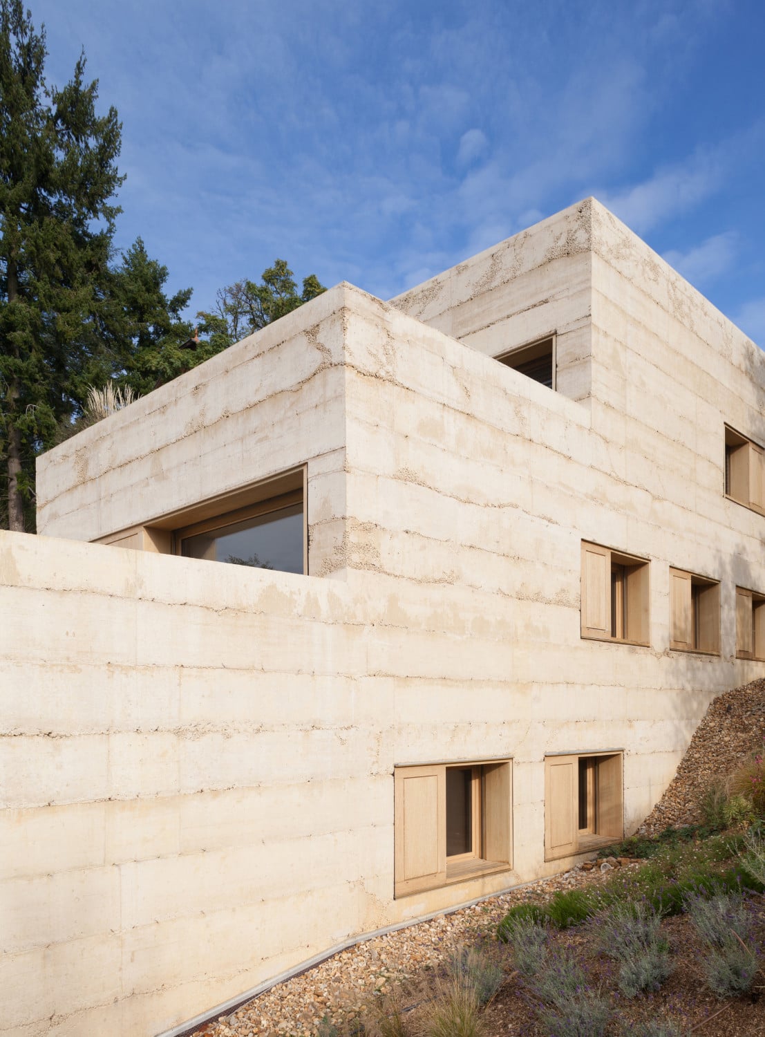 Die Fassade ist in einem sandfarbenen Sichtbeton mit lebendiger Textur ausgeführt.