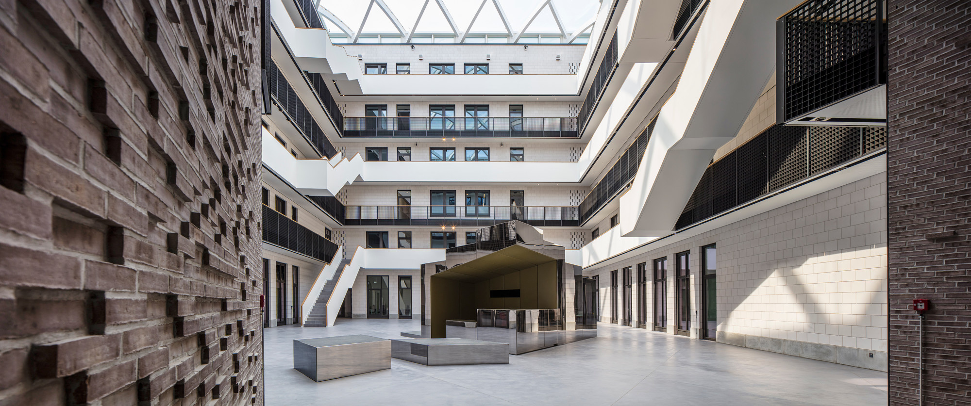 Im Atrium werden Besucher an einem skulpturalen Empfangstresen aus verspiegelten Quadern willkommen geheißen.
