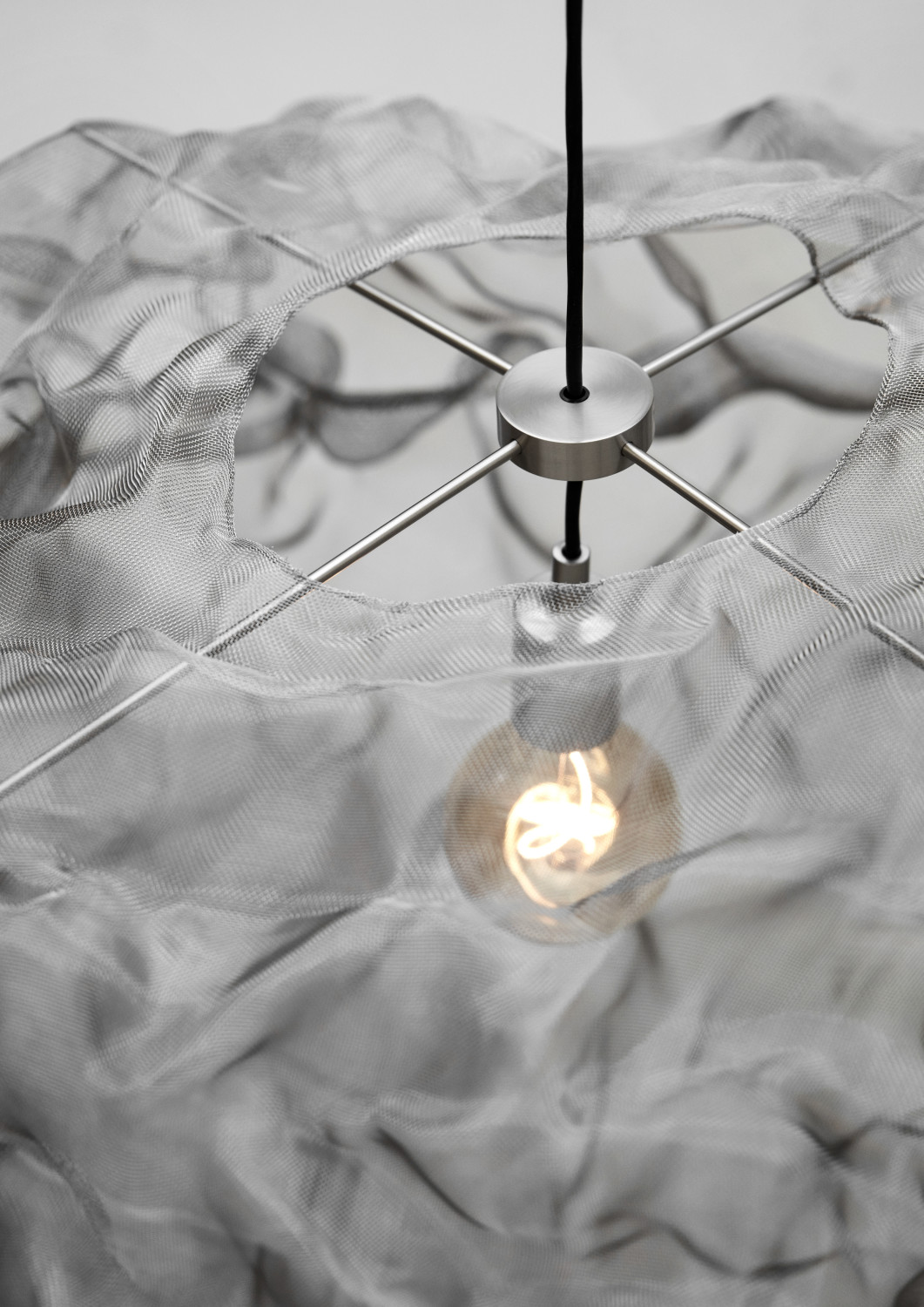 Das semi-transparente Metallnetz lässt einem Blick auf das Leuchtmittel zu und wirkt in seiner Leichtigkeit wie eine schwebende Wolke.
