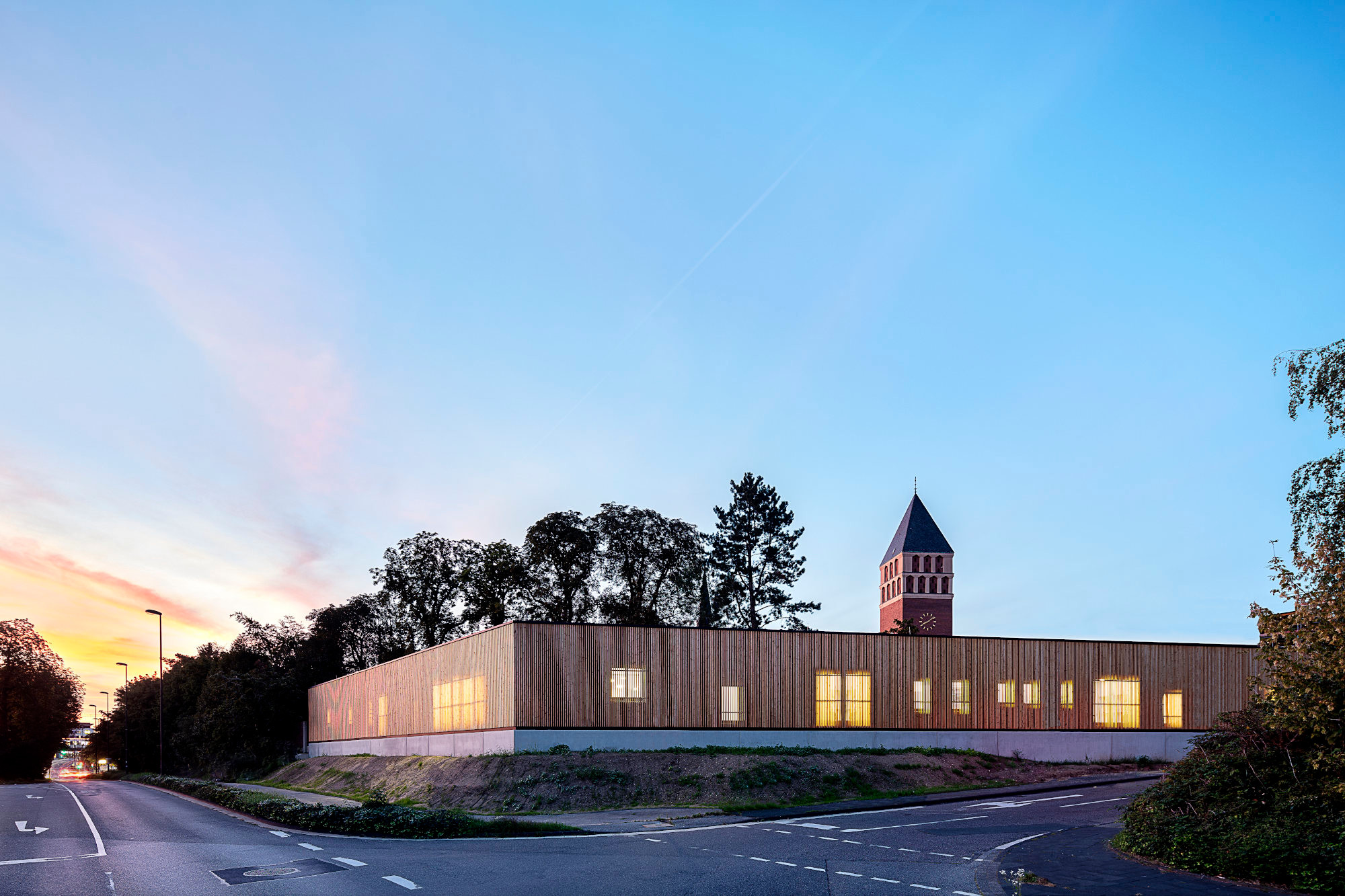 Zur Straße im Süden hingegen erscheint der Baukörper verschlossen, die Holzlamellenfassade aber ist lichtdurchlässig.