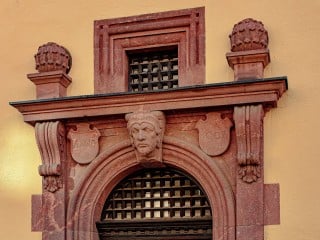 Kartusche mit Segensspruch, Zunftzeichen und stilisiertem Löwenkopf, unten Ranken aus Eichenlaub und Akanthus. Vermutlich hatten auch die nun leeren Flächen auf den Säulenköpfen ursprünglich Reliefs mit symbolischer Darstellung.