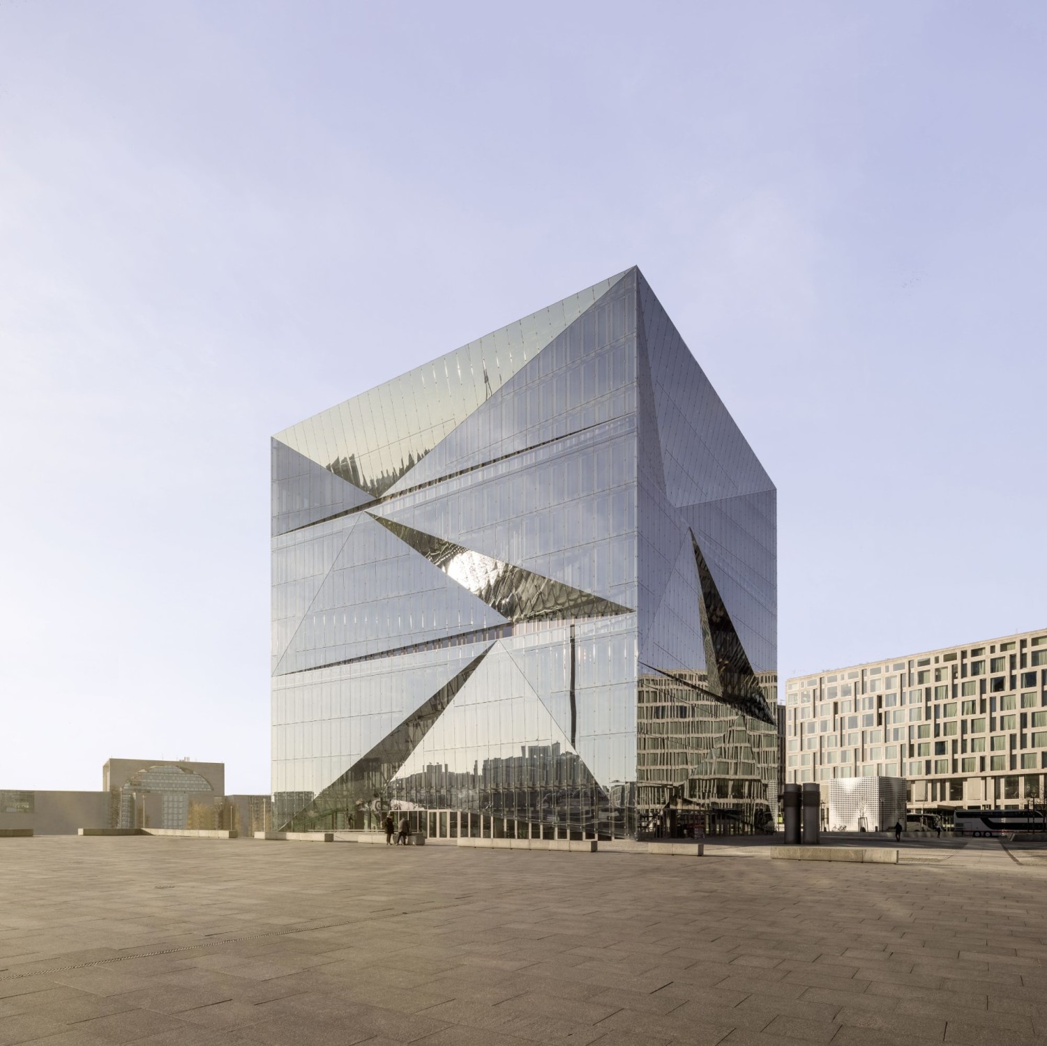 Die vier Fassaden des Quaders verlaufen nicht vertikal, sondern sind mehrfach asymmetrisch gefaltet, sodass sie ein verzerrt gebrochenes Spiegelbild von Himmel und Umgebung erzeugen.