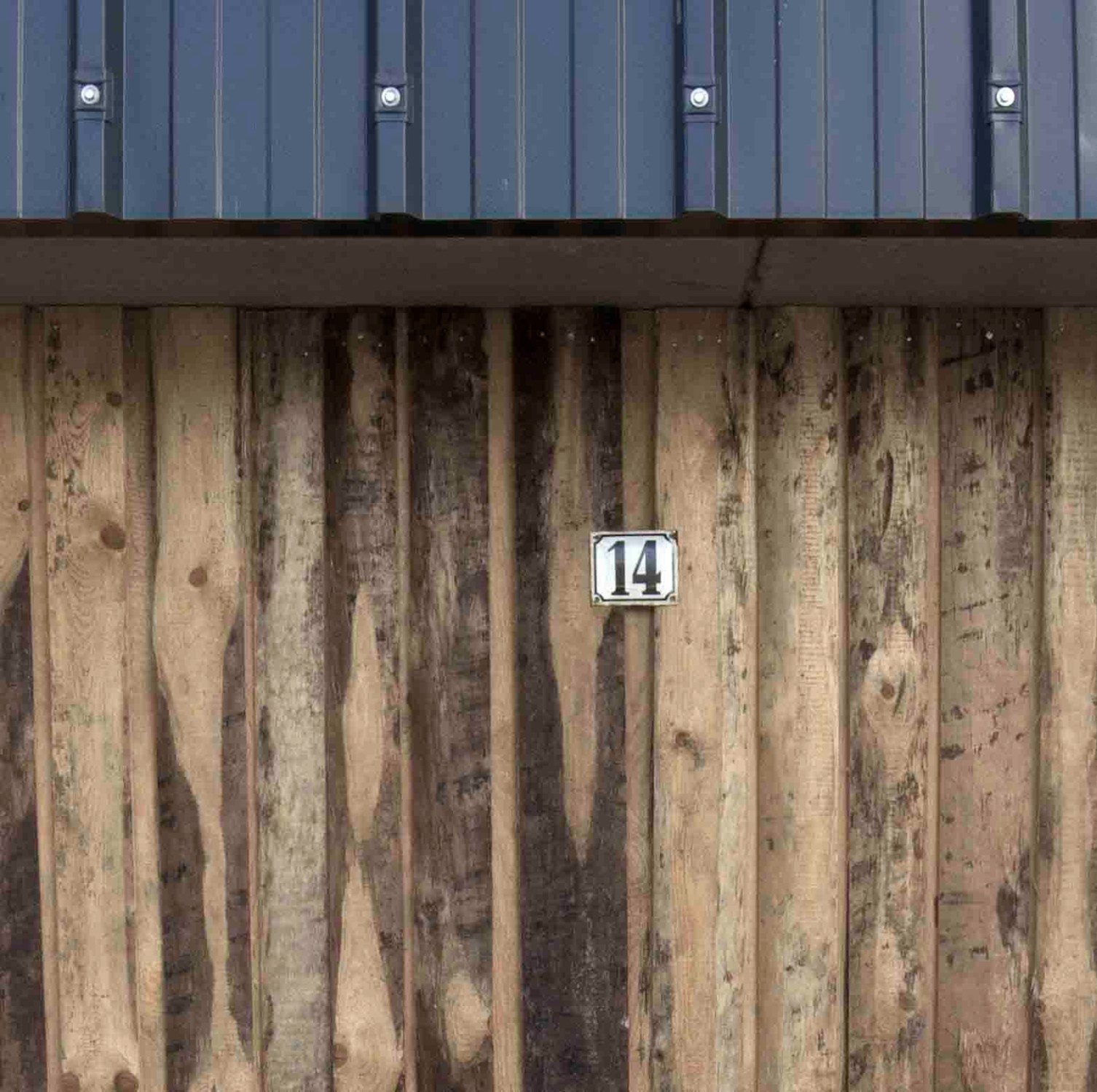 Im leicht zurück versetzten, fensterlosen Erdgeschoss, das als Garage und Technikraum genutzt wird, besteht die Hülle zweiseitig aus Schwartenbrettern, die üblicherweise als Brennholz verwendet werden, da sie teilweise eine Stammrundung haben. 