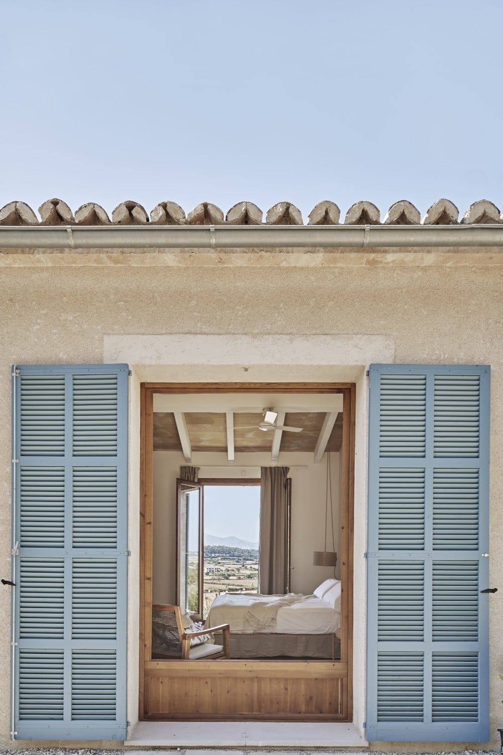 Mit seiner Fassade aus sandfarbenem Naturputz, Fensterläden in Pastellblau und flachem Satteldach mit Ziegeldeckung orientiert sich das Haus an ortstypischer mediterraner Architektur.