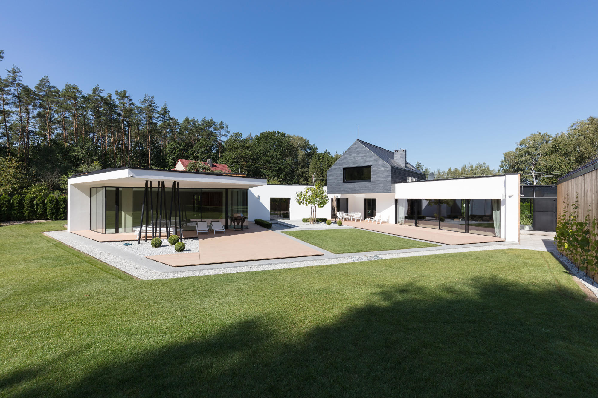 Der eingeschossige, helle Flachbau mit Wohnraum, Küche und diversen Freizeiträumen umfasst einen Hof. In dem mit Schiefer bekleideten, aufgesetzten Obergeschoss befinden sich Schlafraum, Badezimmer und Ankleide.