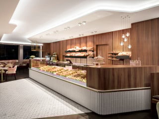 Das Innere des ungefähr zweihundert Quadratmeter großen Kaffeehauses zeichnet sich insgesamt durch klare Linien und organisch-fließende Kurven sowie einen neu interpretierten Mid-Century-Stil aus.