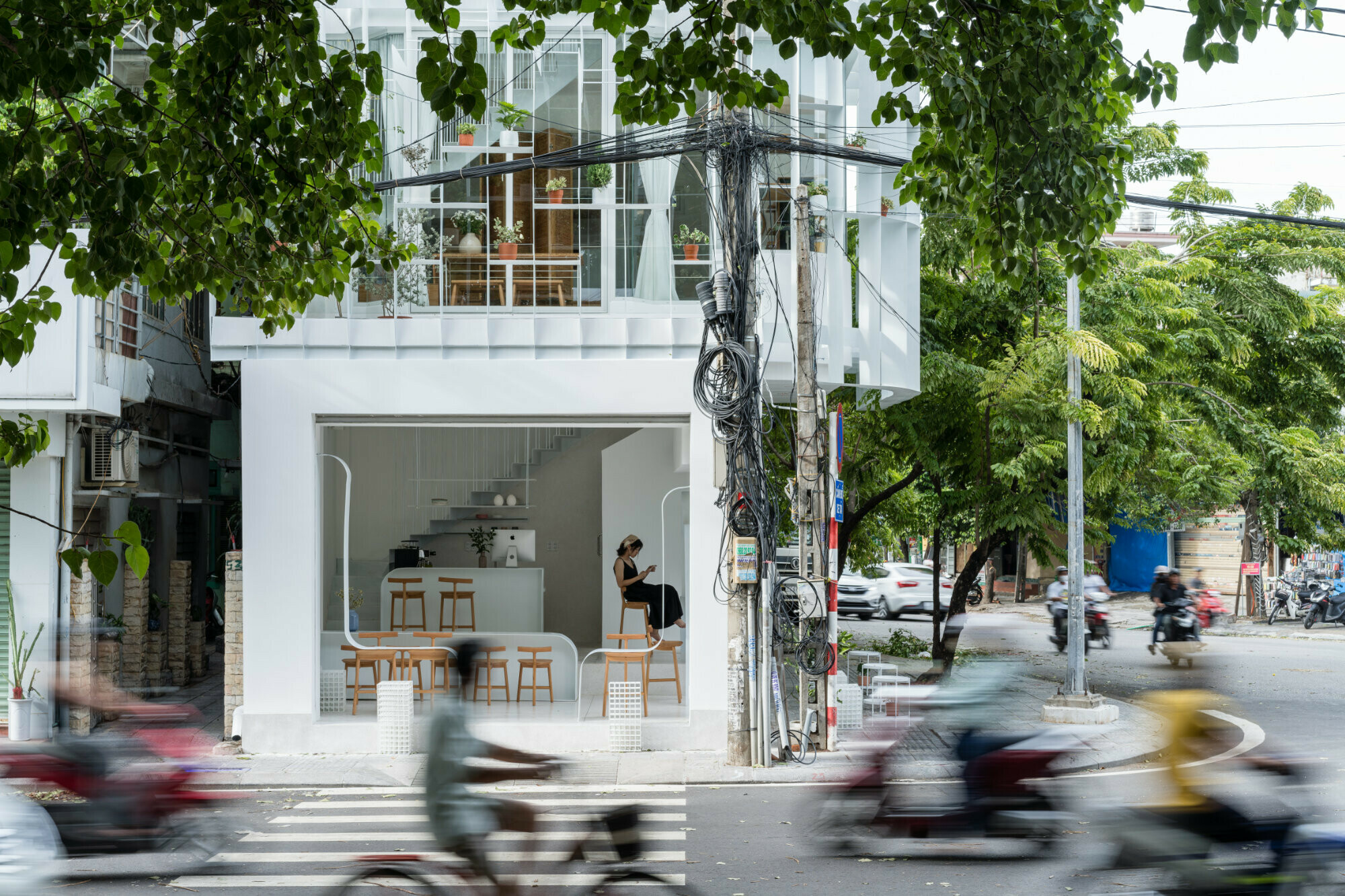 Eine Fassade aus Glas sowie vorgeblendeten weißen Brise-Soleil-Elementen bestimmt nun das äußere Erscheinungsbild des Wohnhauses an einer vielbefahrenen Kreuzung der vietnamesischen Stadt Hue.