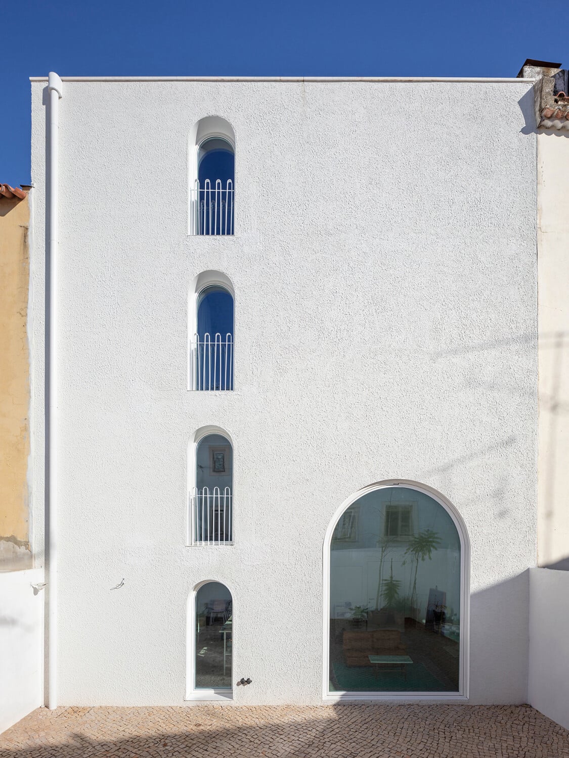 Während sich der Neubau auf dem nur 100 m² großen Grundstück zur Straße mit Blindfenstern zeigt, ist die Fassade zum privaten Patio geöffnet und Bogenfenster lassen Licht ins innere fallen.